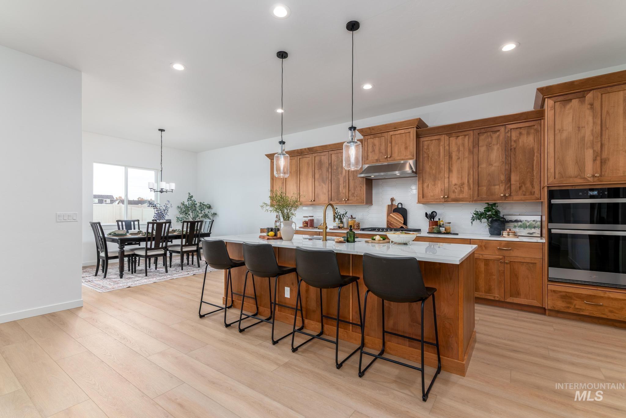 Kitchen featuring brown cabinets, a breakfast bar, pendant lighting, a kitchen island with sink, and recessed lighting