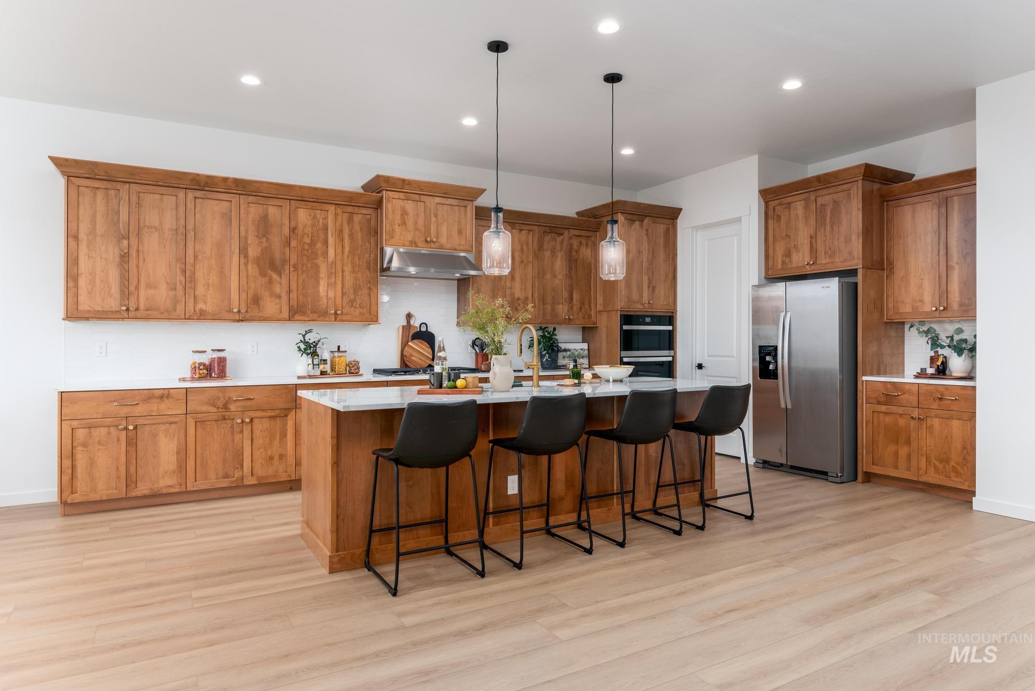 Kitchen featuring brown cabinets, a kitchen breakfast bar, stainless steel appliances, an island with sink, and recessed lighting