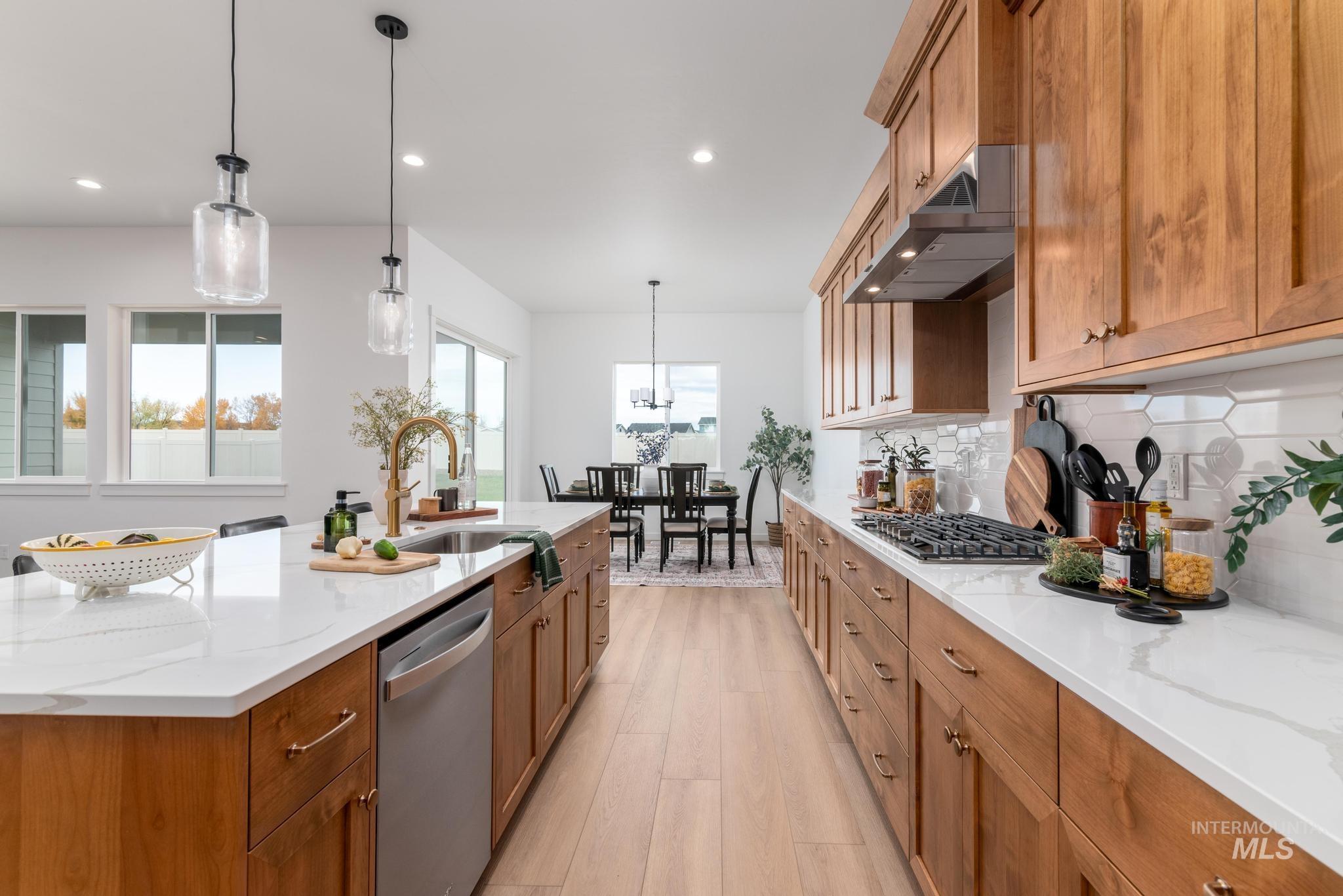 Kitchen with brown cabinets, pendant lighting, light stone counters, stainless steel appliances, and recessed lighting