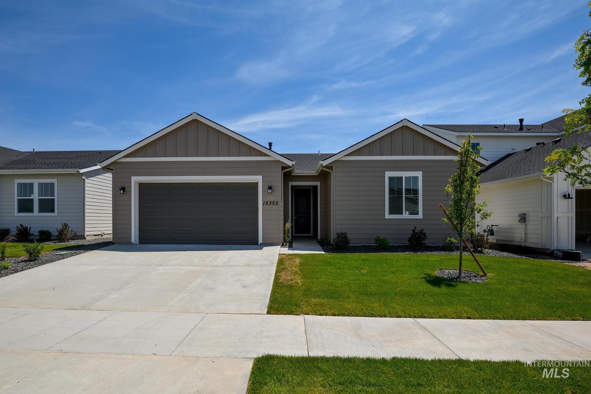 Single story home featuring board and batten siding, a front yard, driveway, and an attached garage