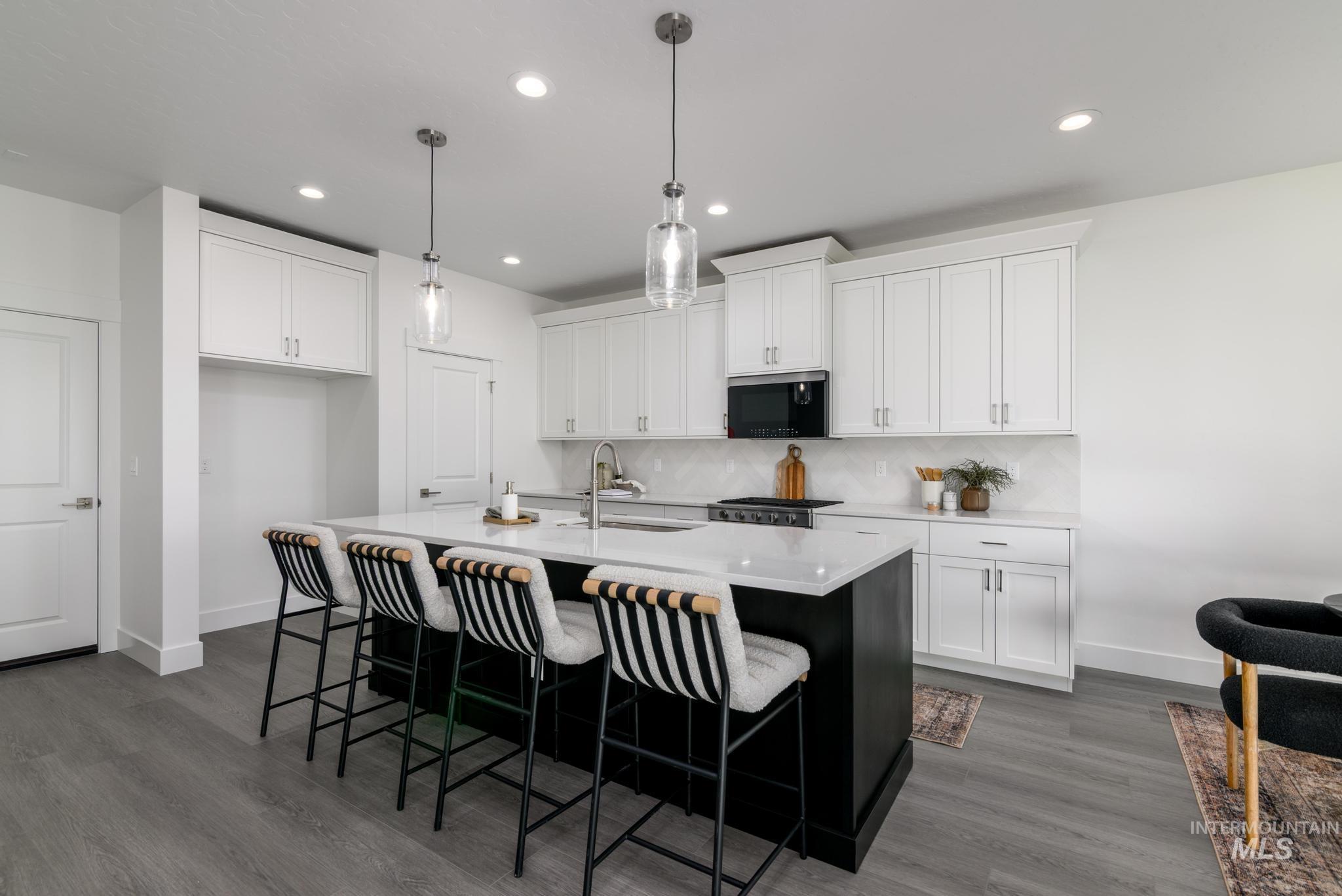 Kitchen featuring an island with sink, white cabinets, light stone counters, decorative light fixtures, and recessed lighting