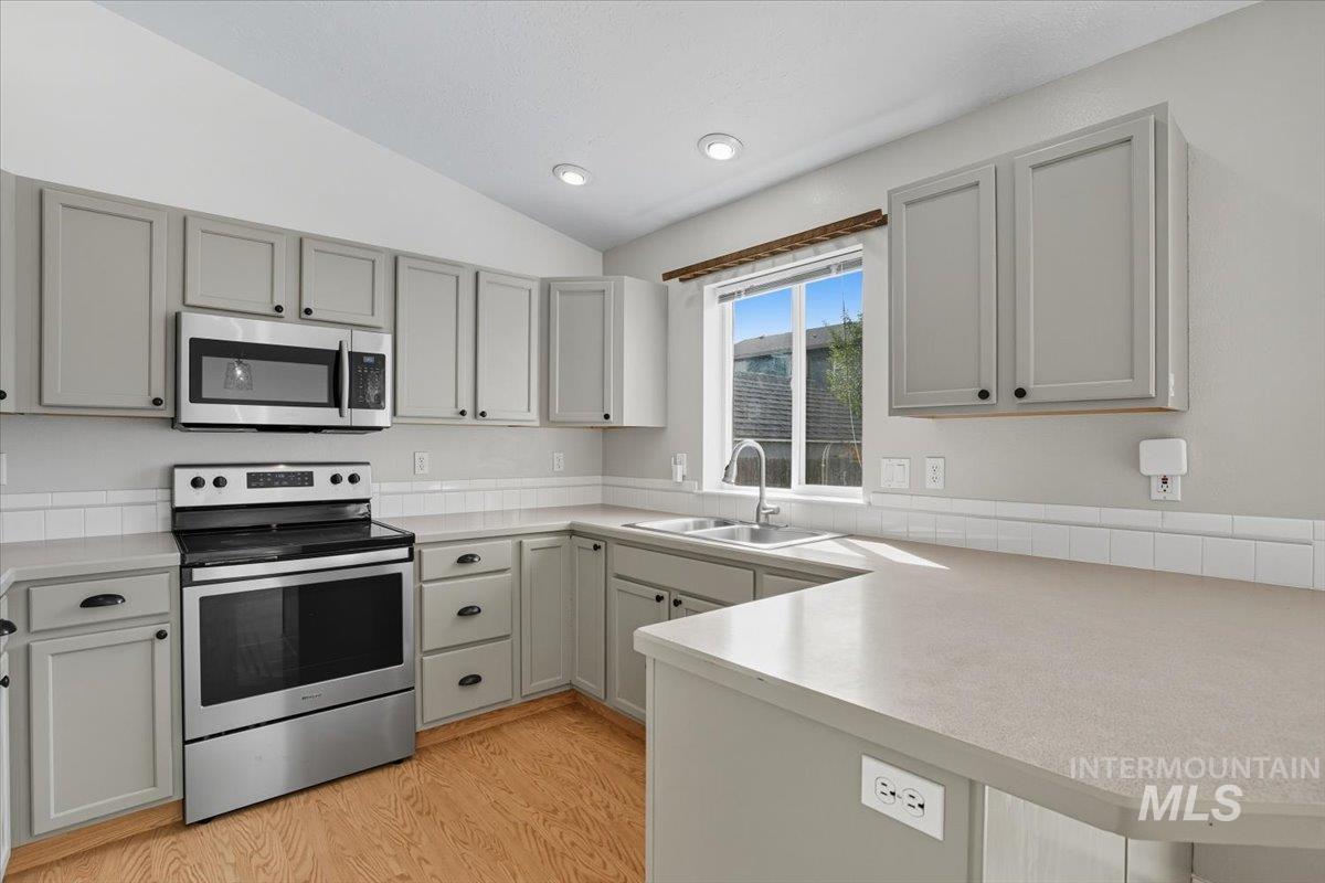 Kitchen featuring appliances with stainless steel finishes, light countertops, vaulted ceiling, light wood-type flooring, and gray cabinets