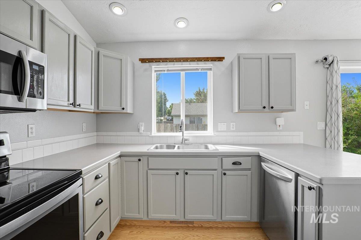 Kitchen featuring stainless steel appliances, light countertops, a peninsula, light wood finished floors, and a textured ceiling