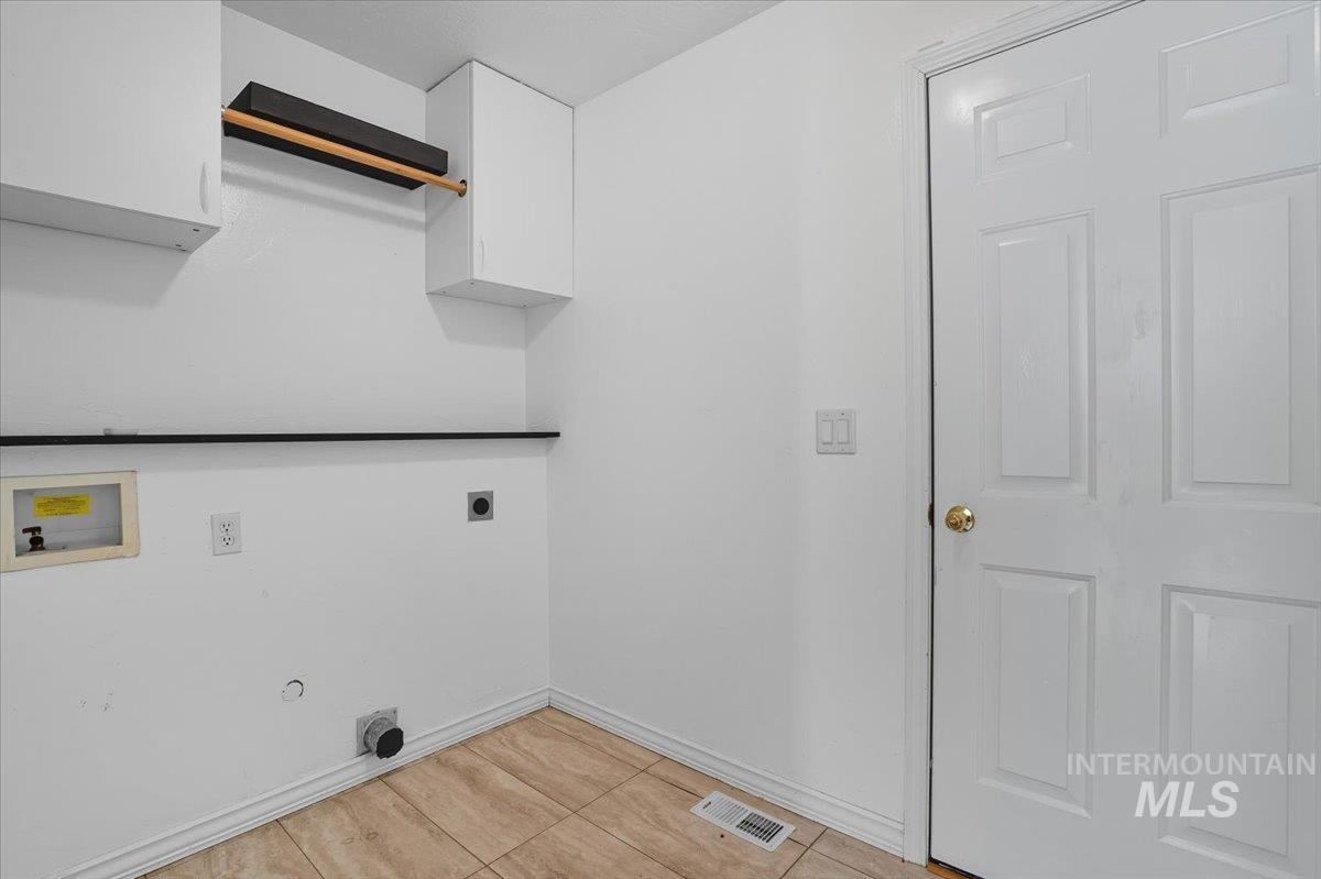 Laundry area featuring electric dryer hookup, washer hookup, light tile patterned floors, and cabinet space
