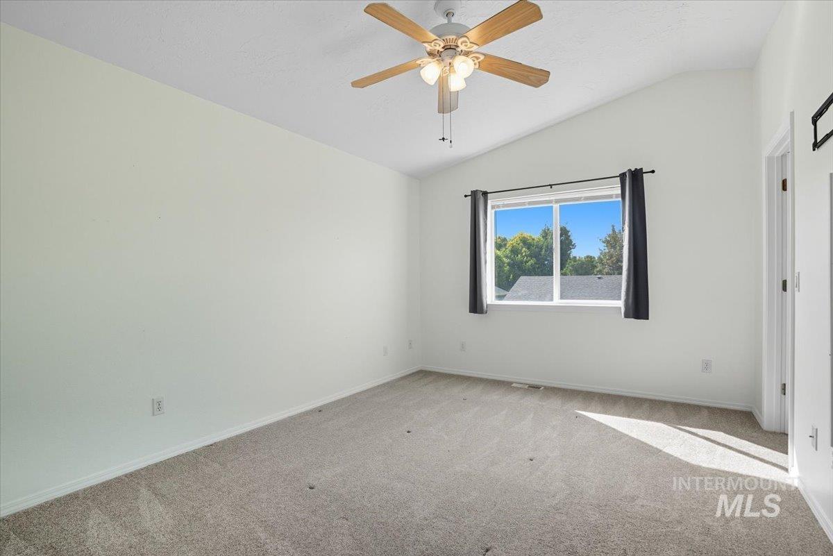 Carpeted empty room with vaulted ceiling and a ceiling fan
