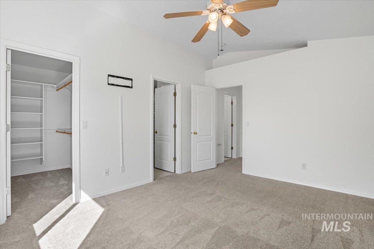 Unfurnished bedroom with light carpet, a walk in closet, vaulted ceiling, and ceiling fan