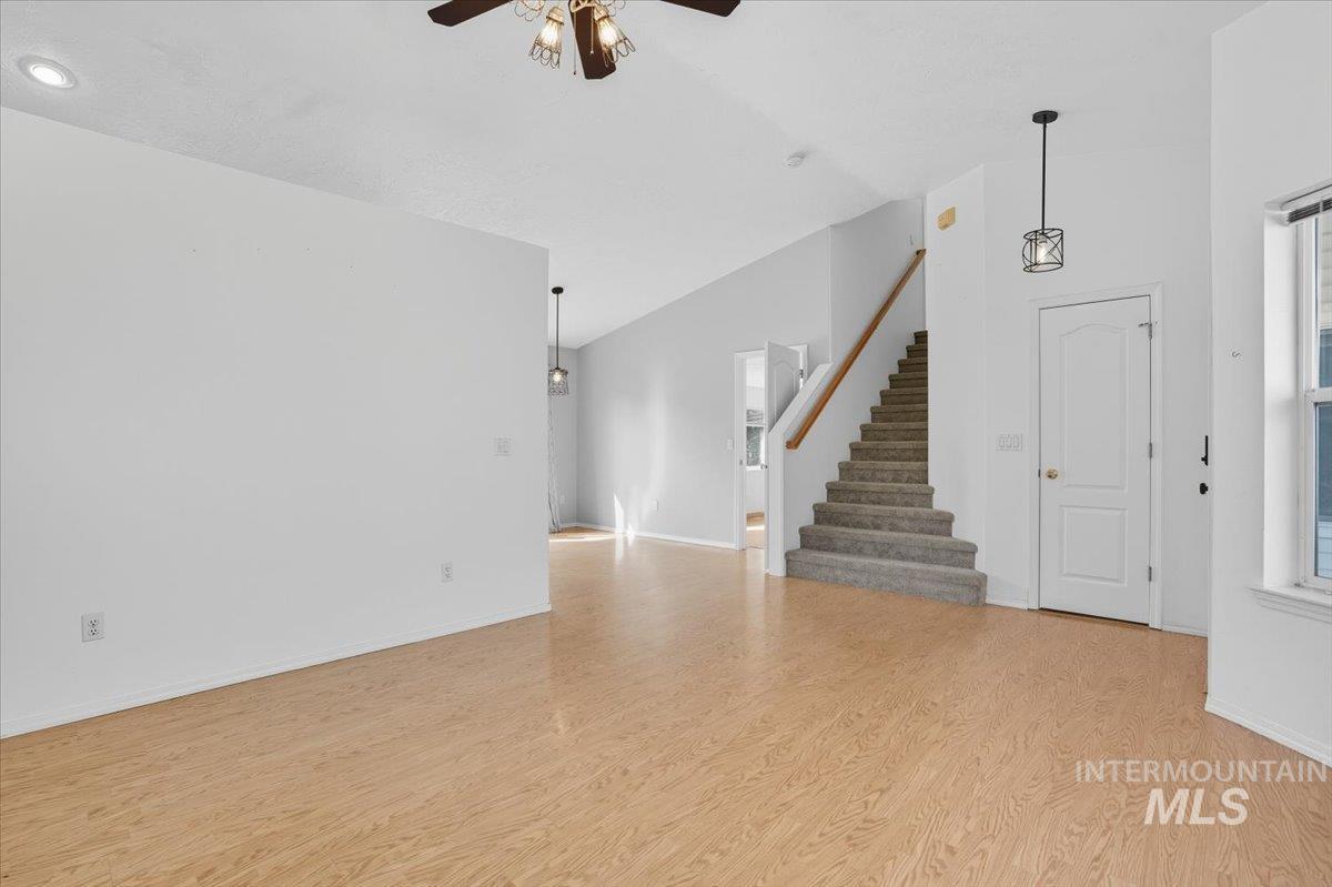 Unfurnished living room with light wood-type flooring, stairs, ceiling fan, and lofted ceiling