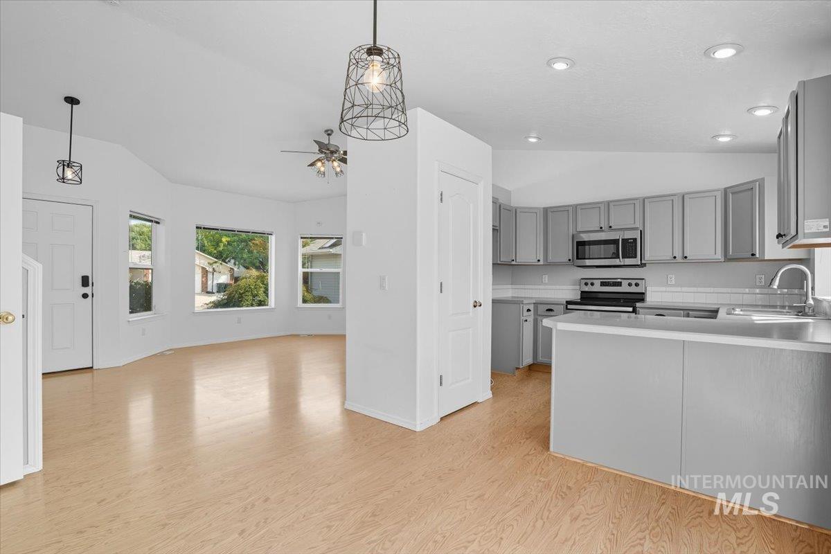 Kitchen with gray cabinets, lofted ceiling, light countertops, light wood-style flooring, and a peninsula