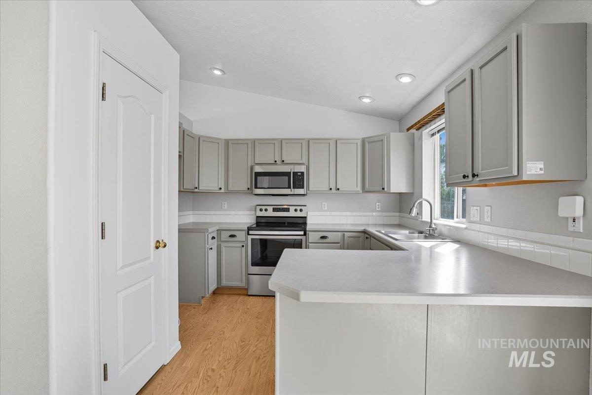 Kitchen featuring appliances with stainless steel finishes, light countertops, a peninsula, lofted ceiling, and gray cabinets