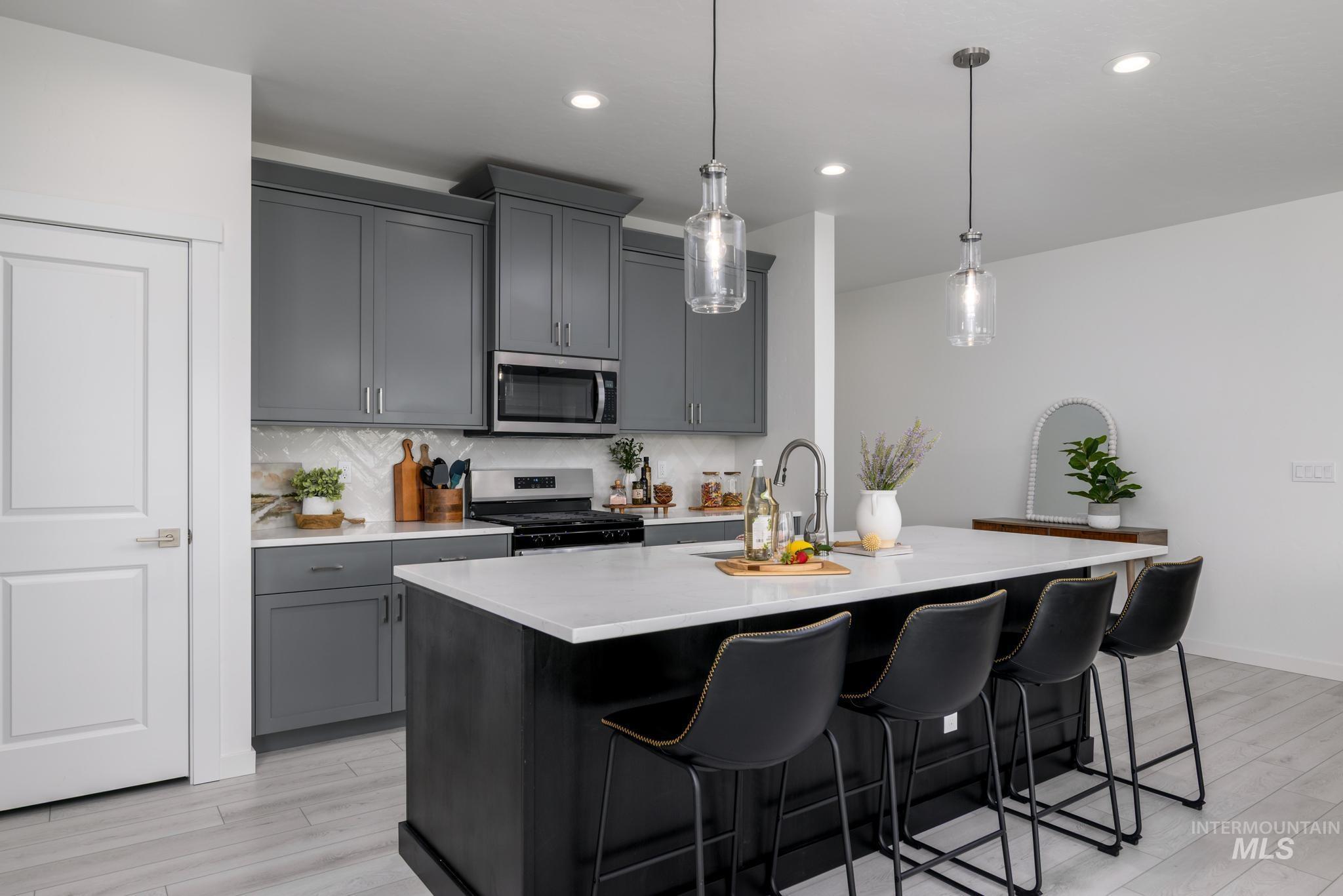 Kitchen with tasteful backsplash, decorative light fixtures, appliances with stainless steel finishes, a breakfast bar area, and a center island with sink