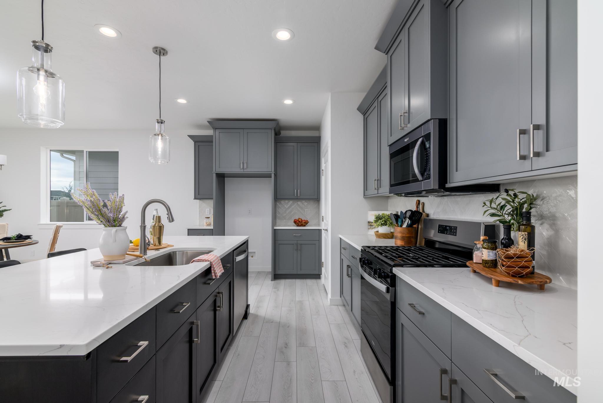 Kitchen featuring appliances with stainless steel finishes, pendant lighting, light stone counters, a center island with sink, and backsplash