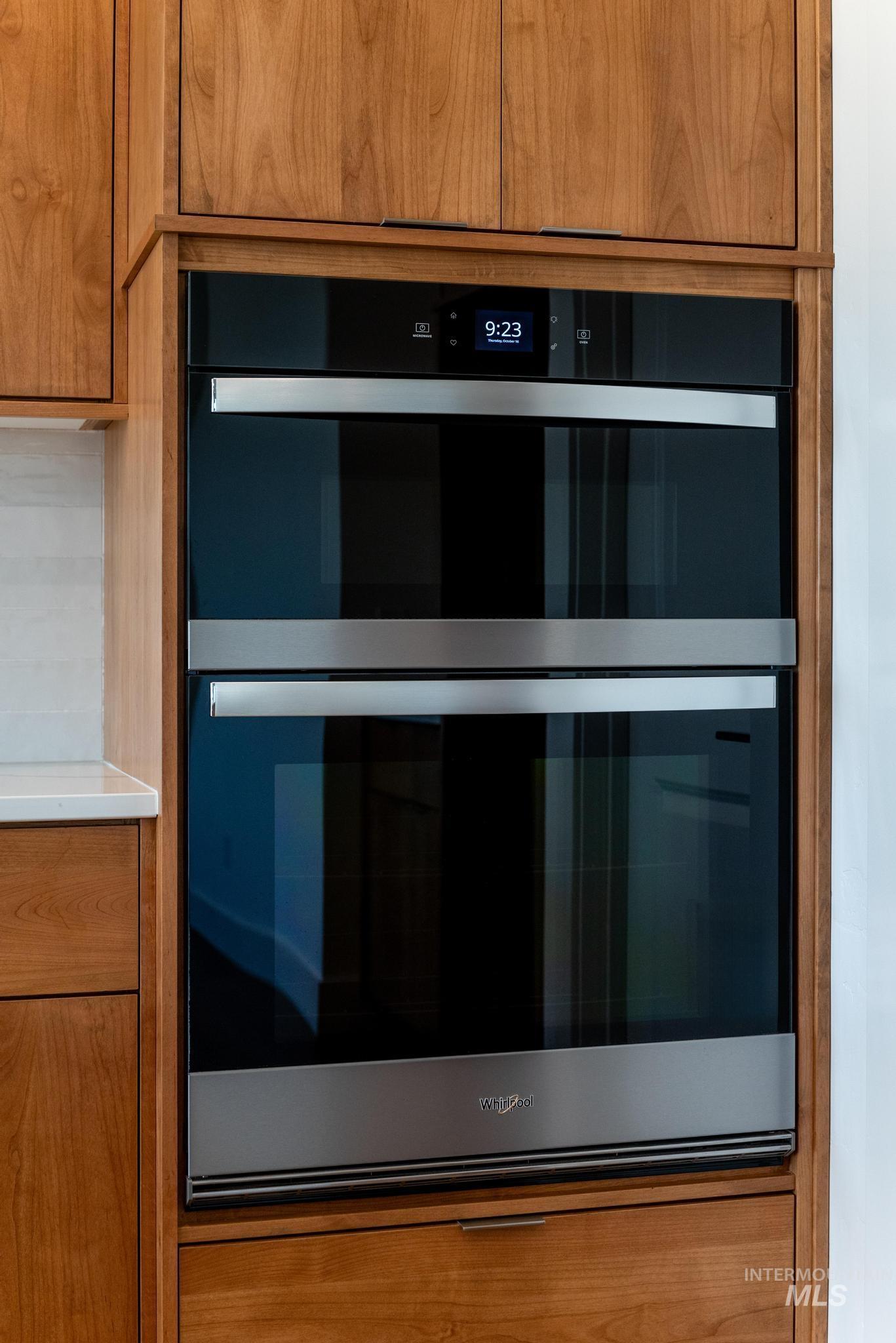 Detailed view of brown cabinetry, stainless steel double oven, and light countertops