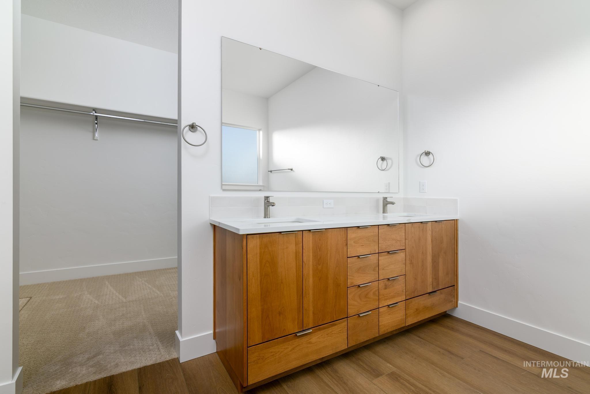 Full bathroom with double vanity, a walk in closet, and light wood finished floors