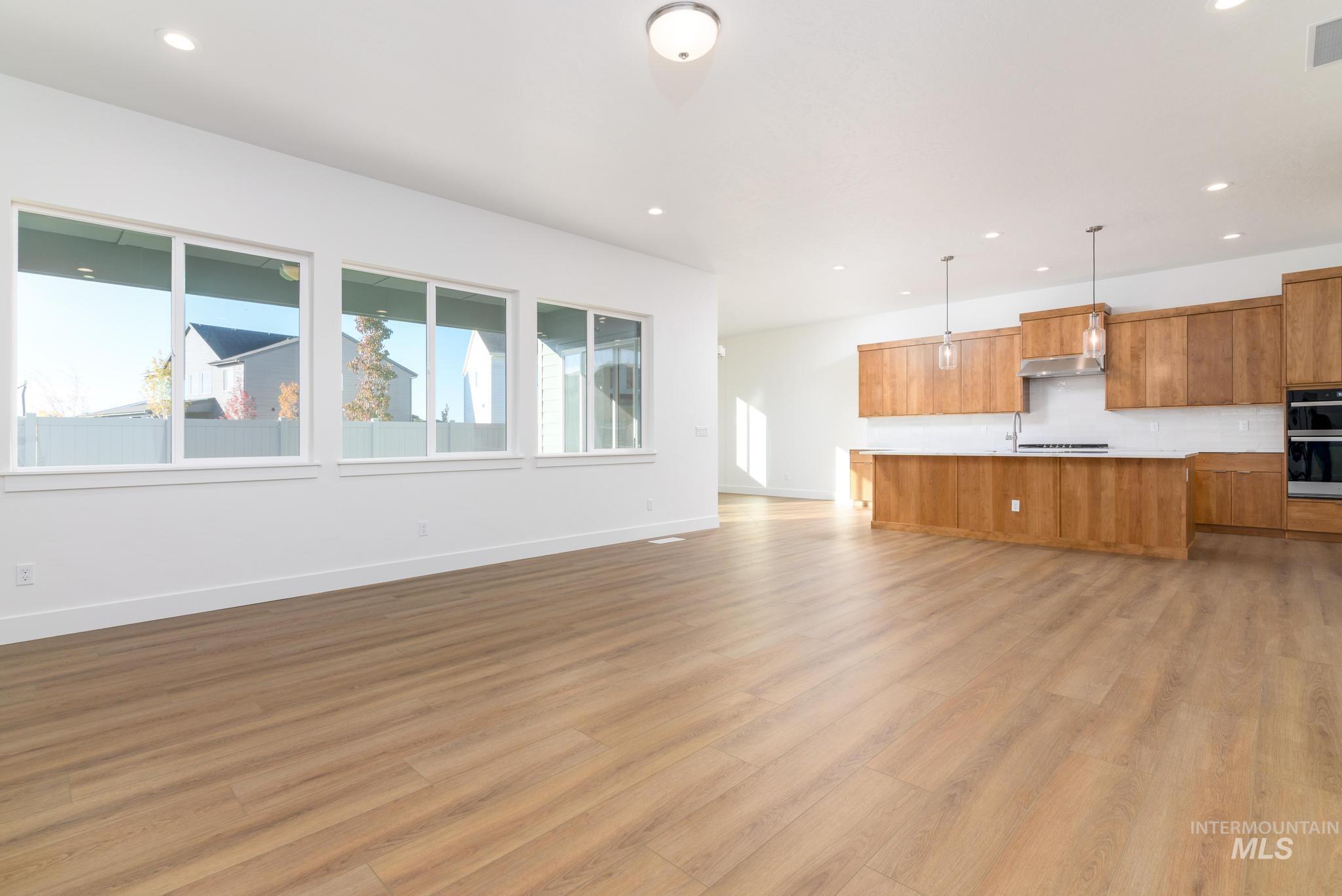 Kitchen featuring brown cabinetry, open floor plan, light countertops, a kitchen island with sink, and pendant lighting