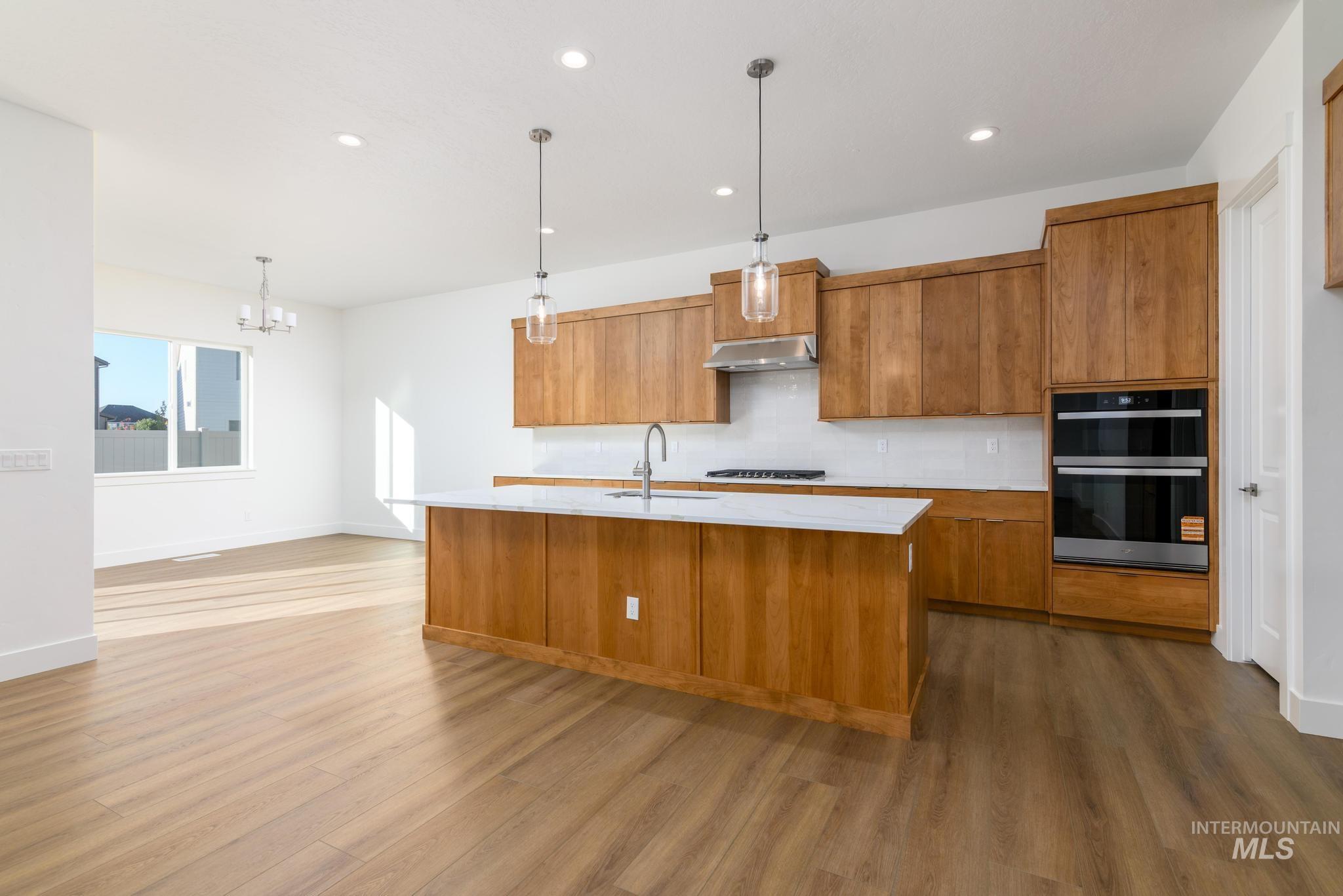 Kitchen with brown cabinetry, a center island with sink, decorative light fixtures, and recessed lighting