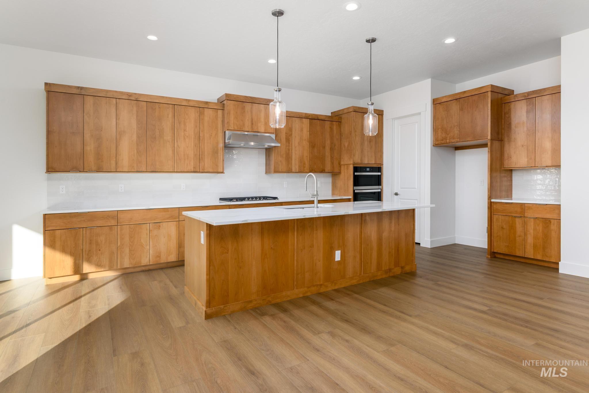 Kitchen featuring decorative backsplash, hanging light fixtures, brown cabinets, a kitchen island with sink, and double wall oven
