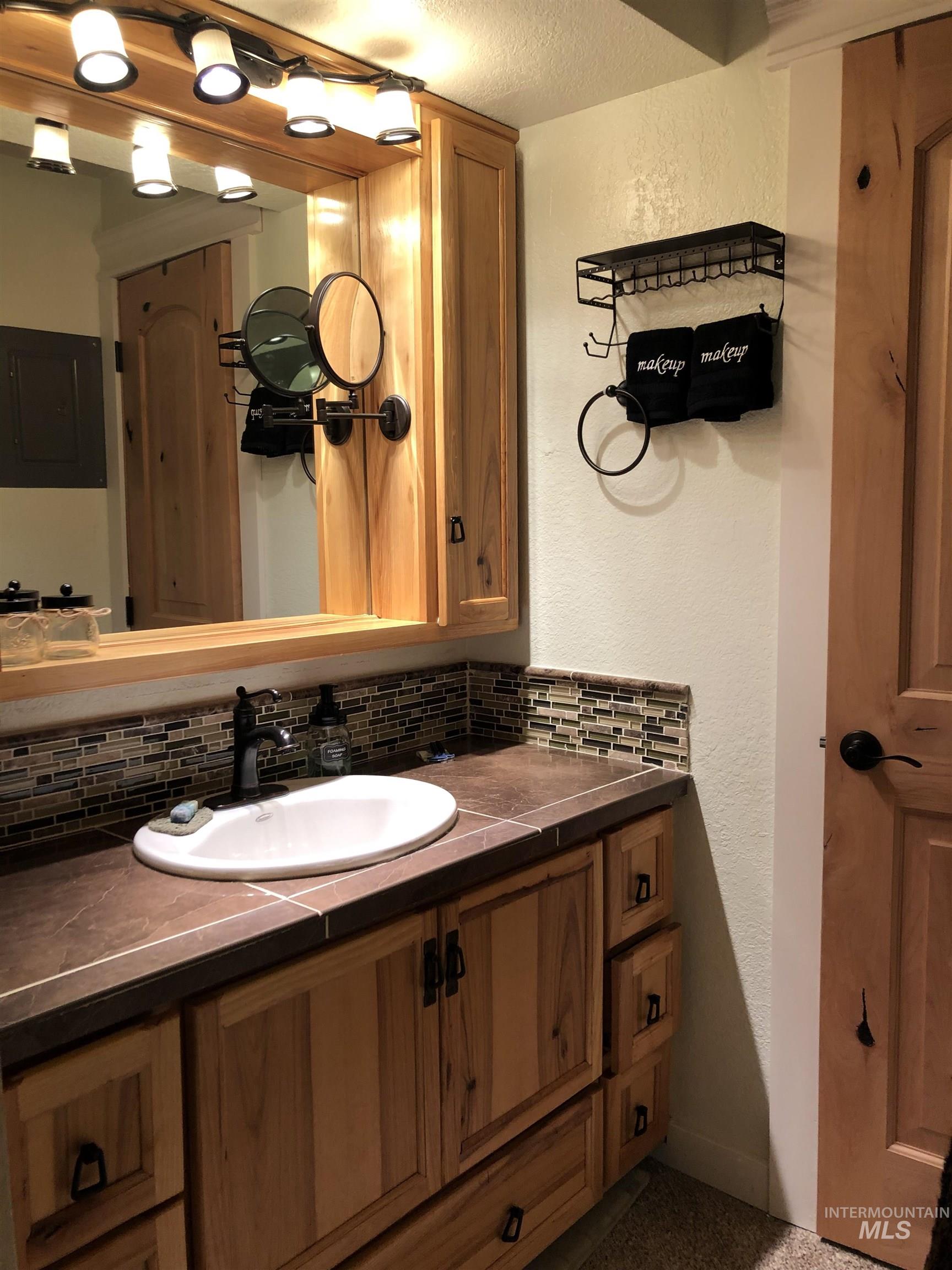 Bathroom featuring vanity, electric panel, a textured wall, decorative backsplash, and a textured ceiling