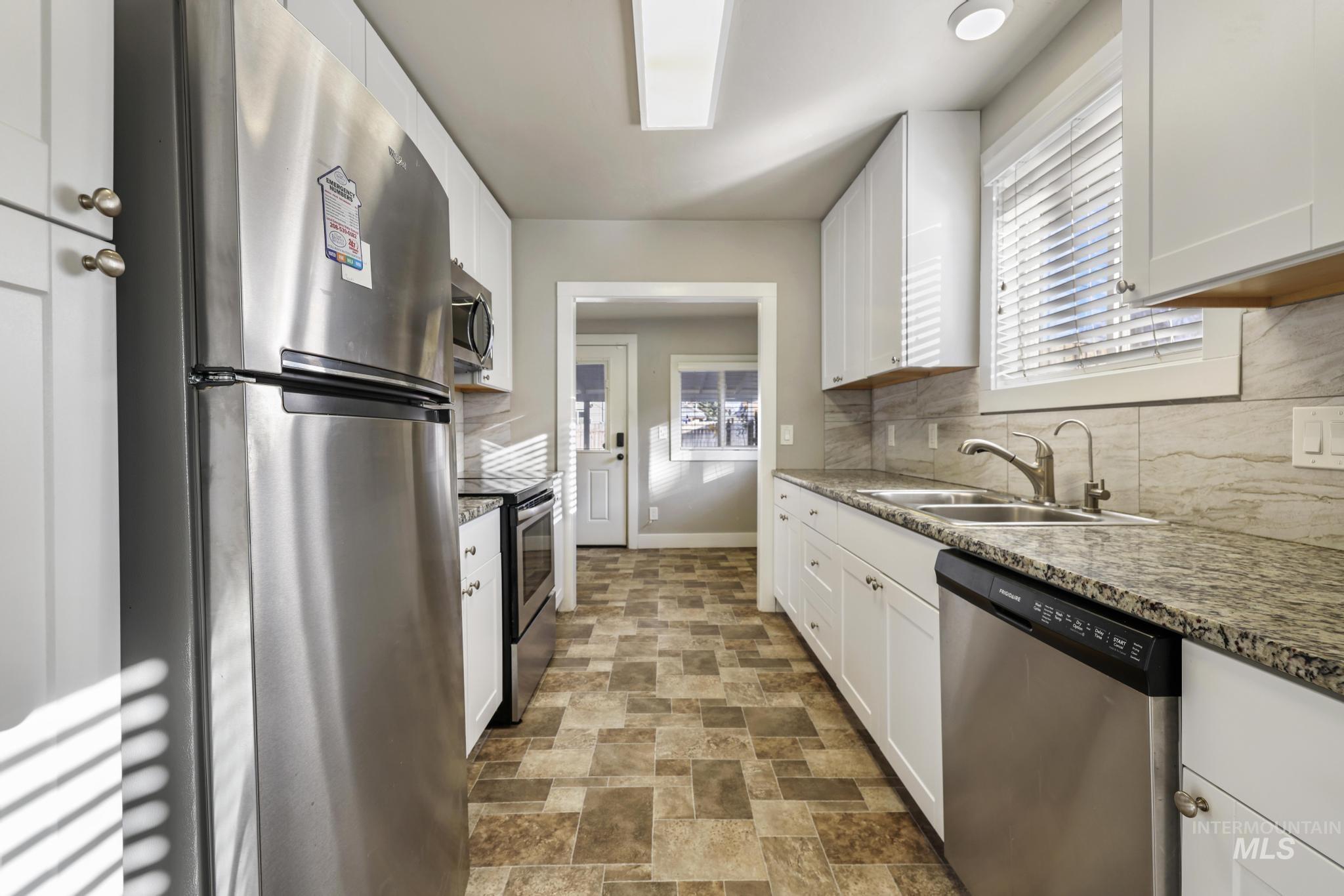 Kitchen with appliances with stainless steel finishes, white cabinets, tasteful backsplash, and stone finish floors