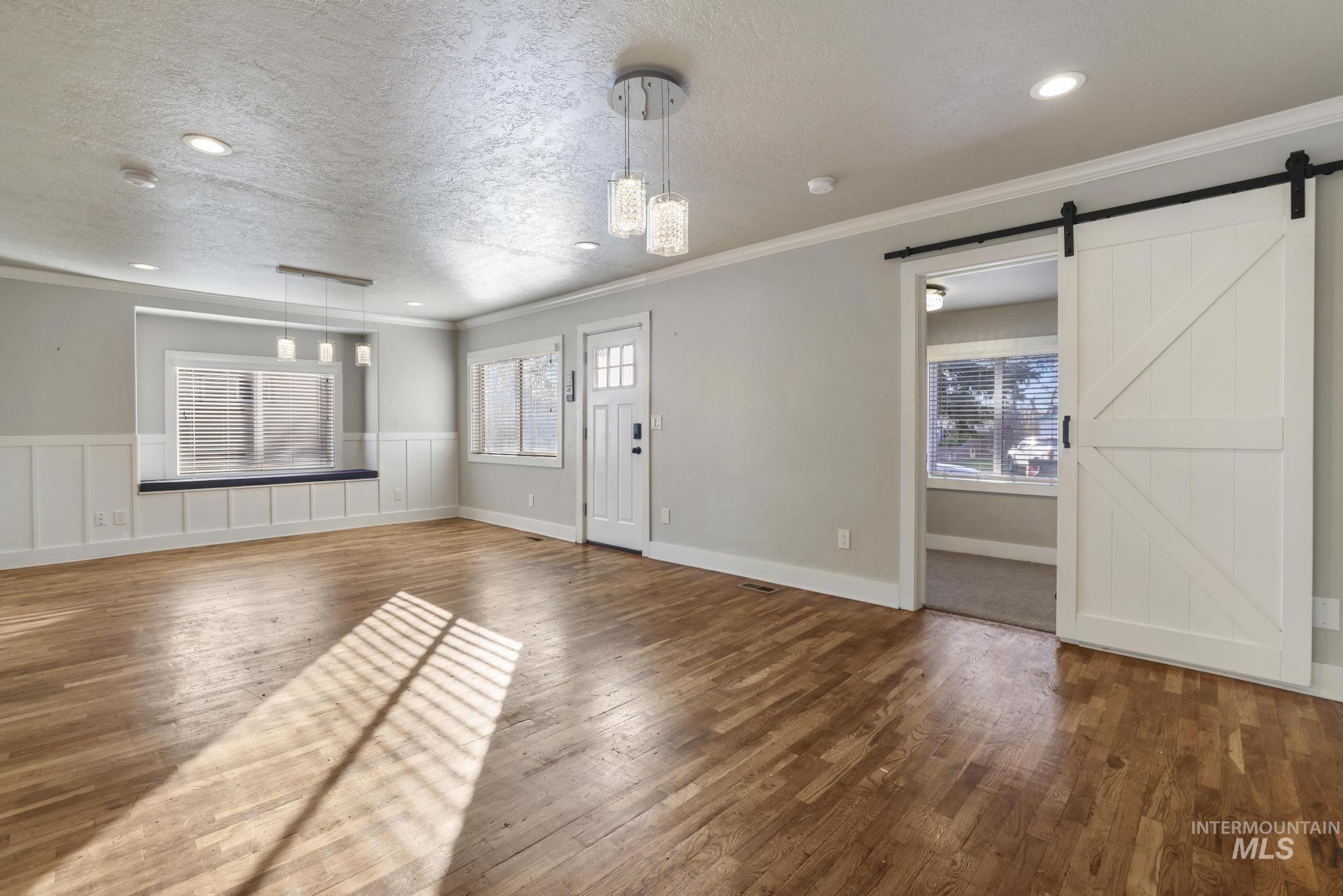 Unfurnished living room featuring a textured ceiling, recessed lighting, wood-type flooring, crown molding, and a barn door