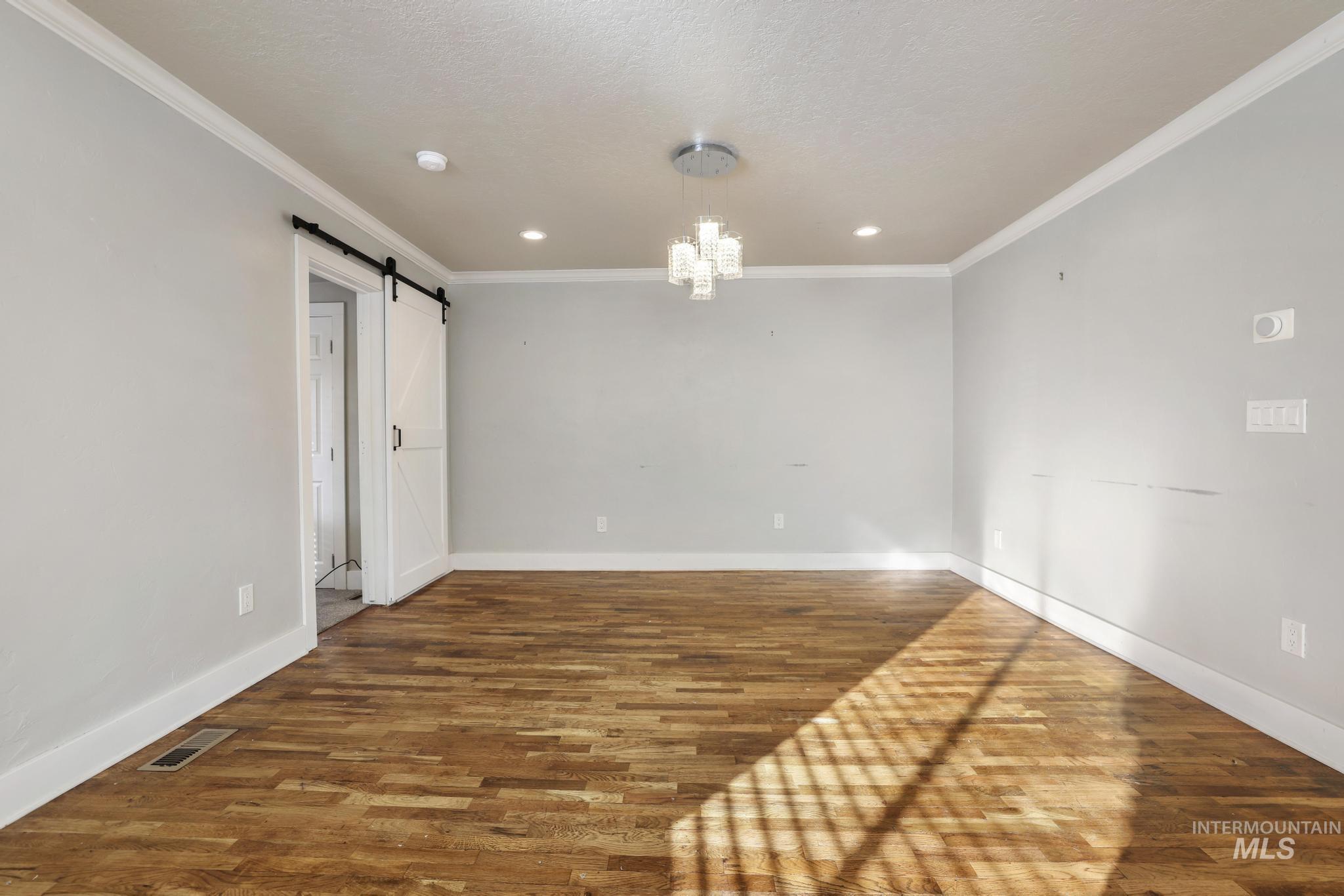 Spare room with wood finished floors, a barn door, a chandelier, ornamental molding, and recessed lighting