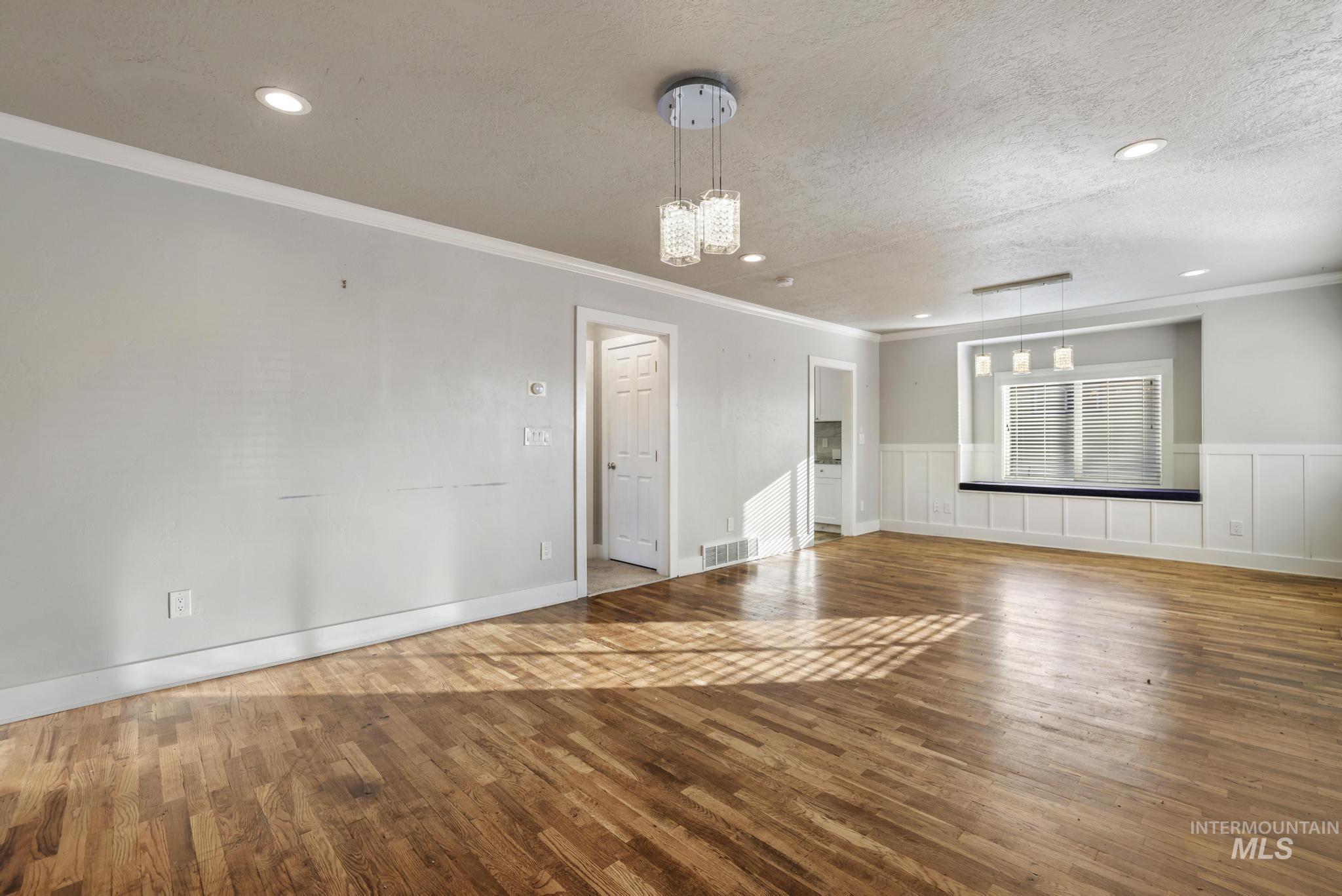 Spare room featuring hardwood / wood-style flooring, a wainscoted wall, a textured ceiling, a chandelier, and recessed lighting