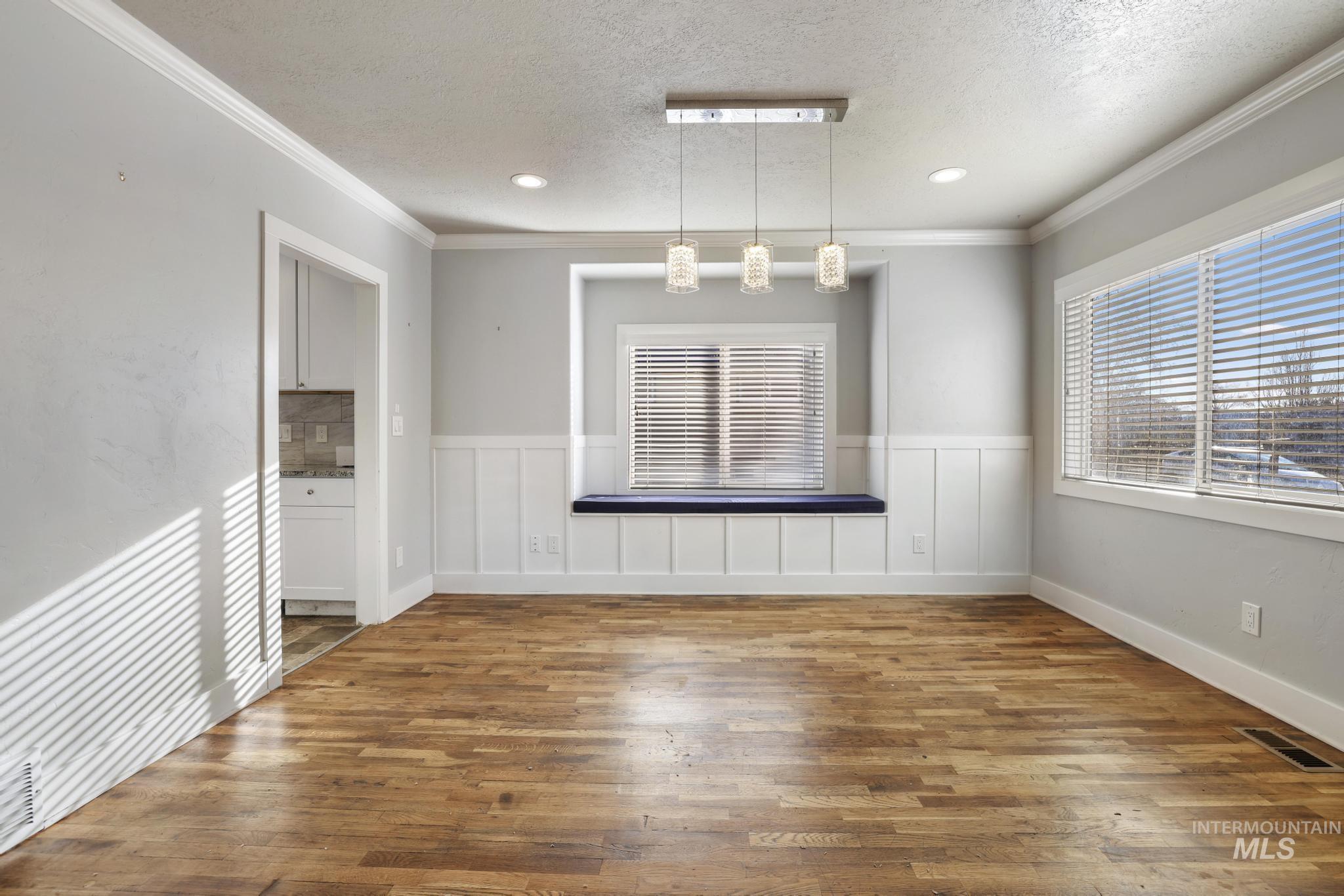 Unfurnished dining area with hardwood / wood-style flooring, a textured ceiling, recessed lighting, ornamental molding, and a wainscoted wall