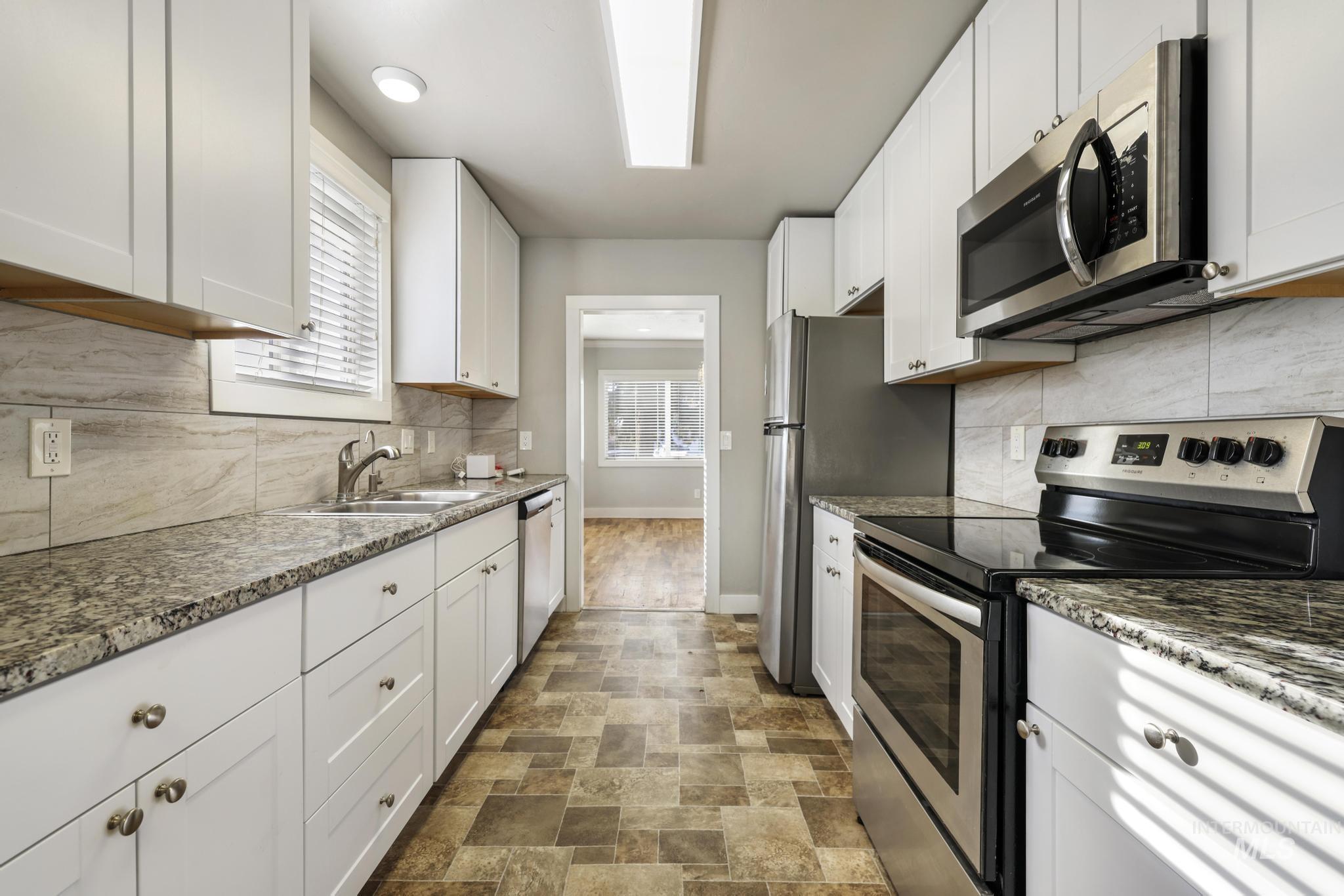 Kitchen featuring stainless steel appliances, white cabinets, stone finish floors, and backsplash