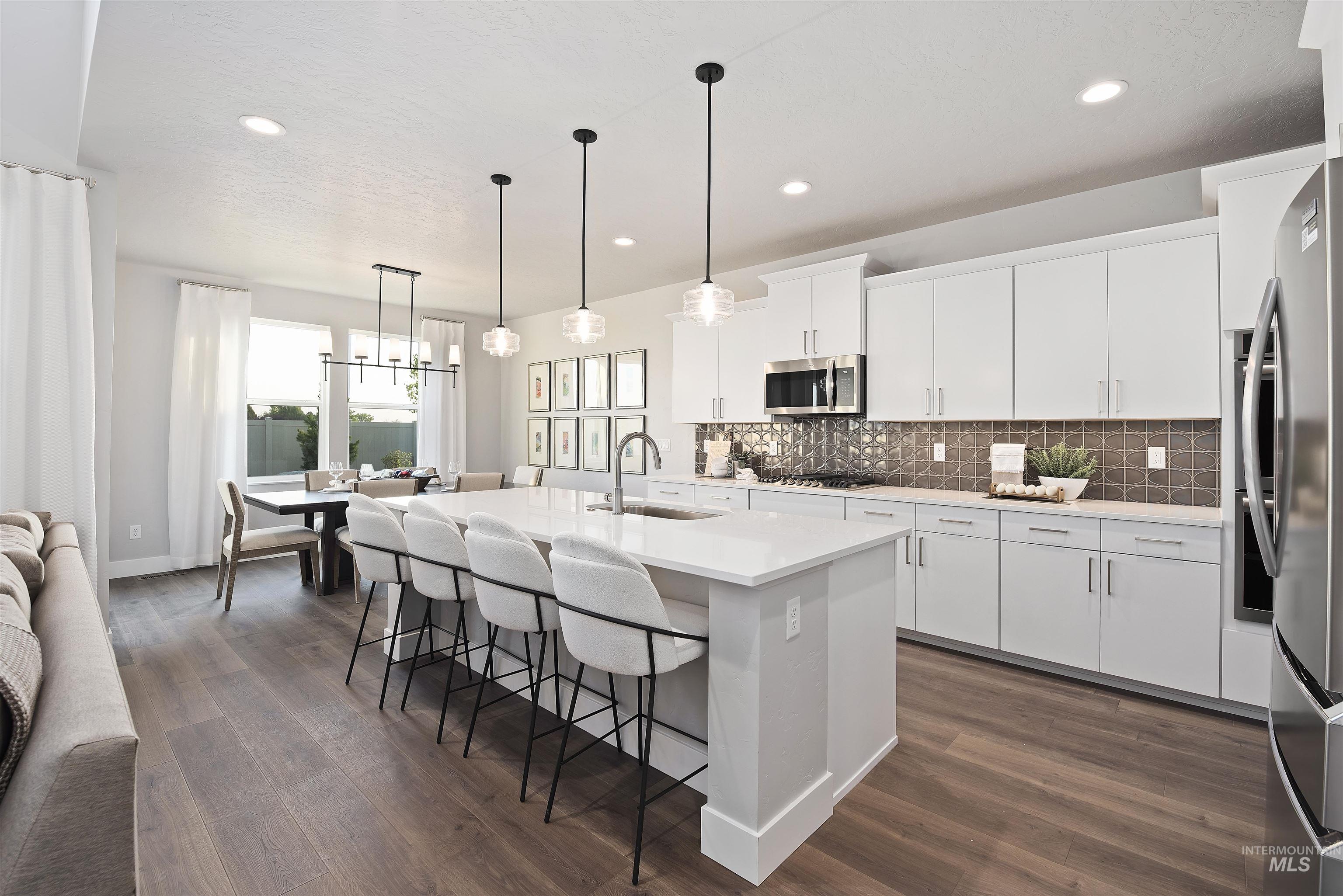 Kitchen with decorative backsplash, a breakfast bar area, an island with sink, white cabinetry, and decorative light fixtures