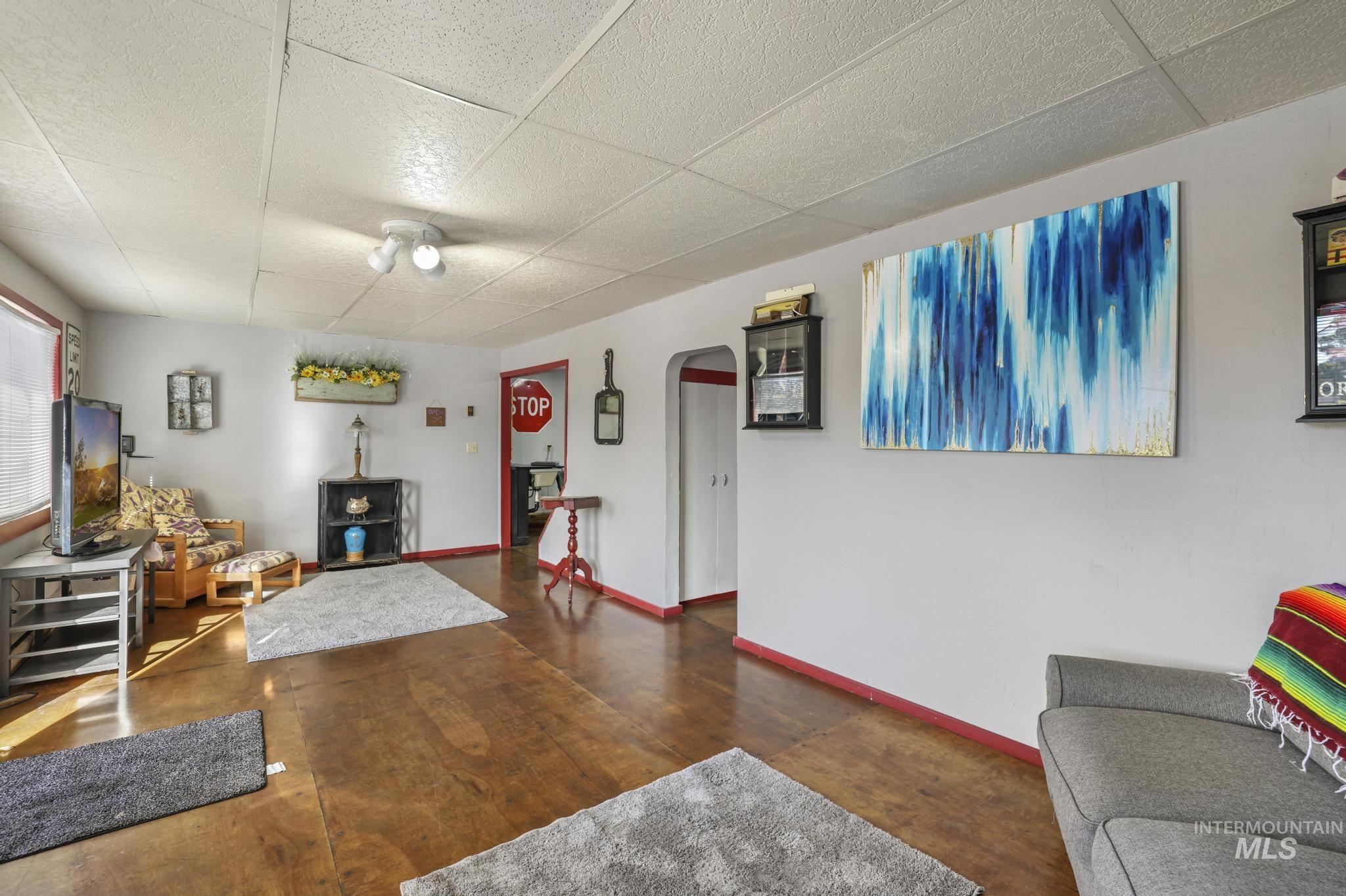 Living area featuring arched walkways, a drop ceiling, finished concrete flooring, and a wood stove