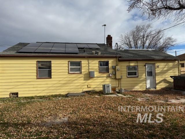 Back of house with roof mounted solar panels and a chimney
