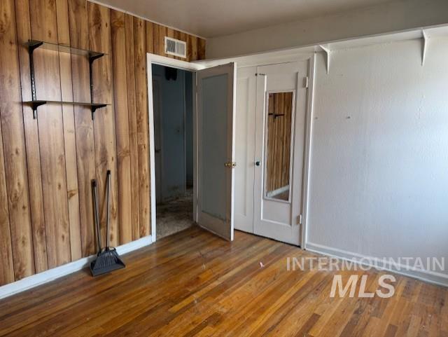 Unfurnished bedroom featuring hardwood / wood-style floors and wood walls