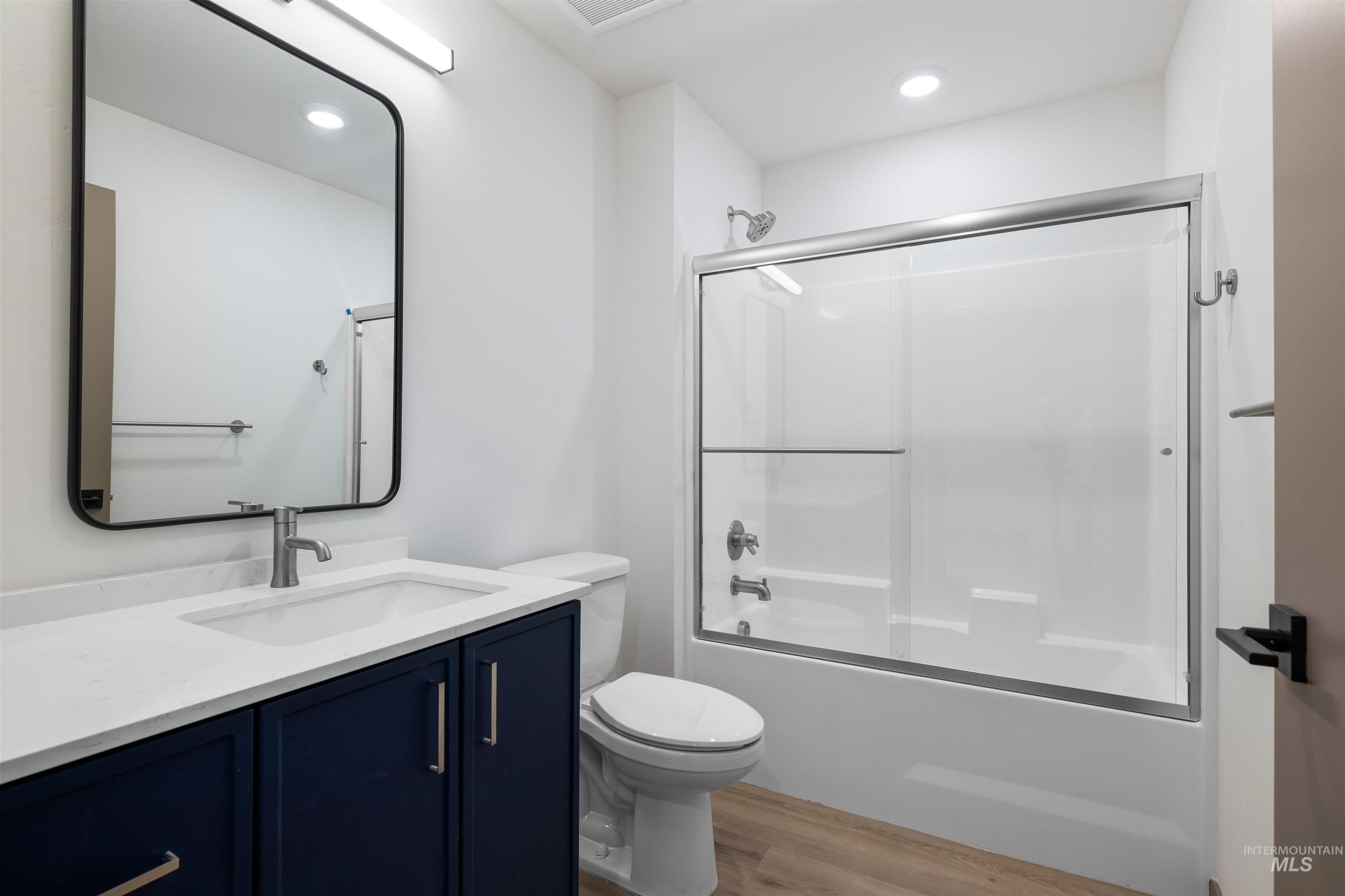 Full bath featuring vanity, combined bath / shower with glass door, light wood finished floors, and recessed lighting