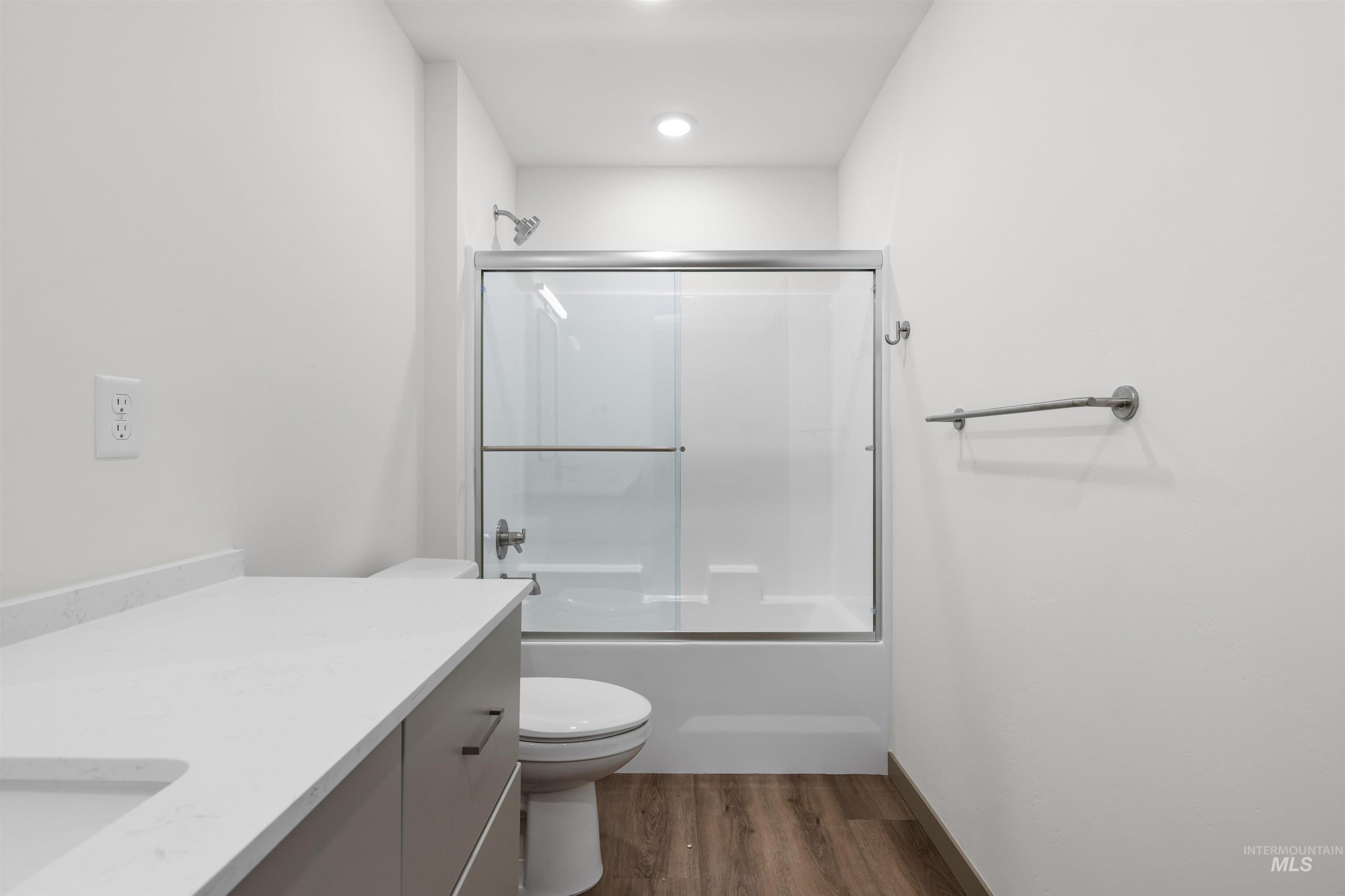 Bathroom featuring bath / shower combo with glass door, vanity, and dark wood-style flooring