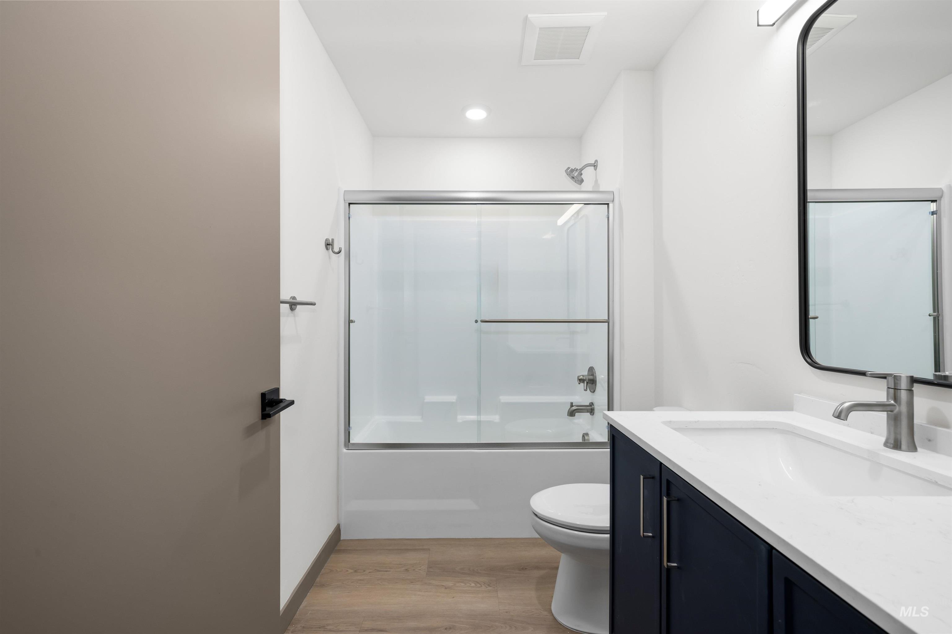 Bathroom with vanity, shower / bath combination with glass door, and light wood-type flooring