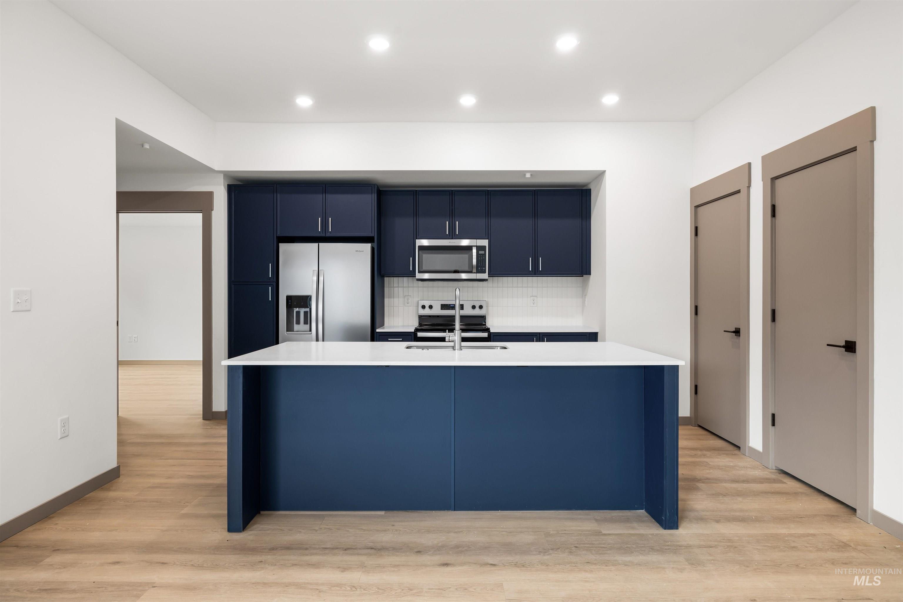 Kitchen featuring blue cabinets, tasteful backsplash, appliances with stainless steel finishes, light wood-style flooring, and recessed lighting
