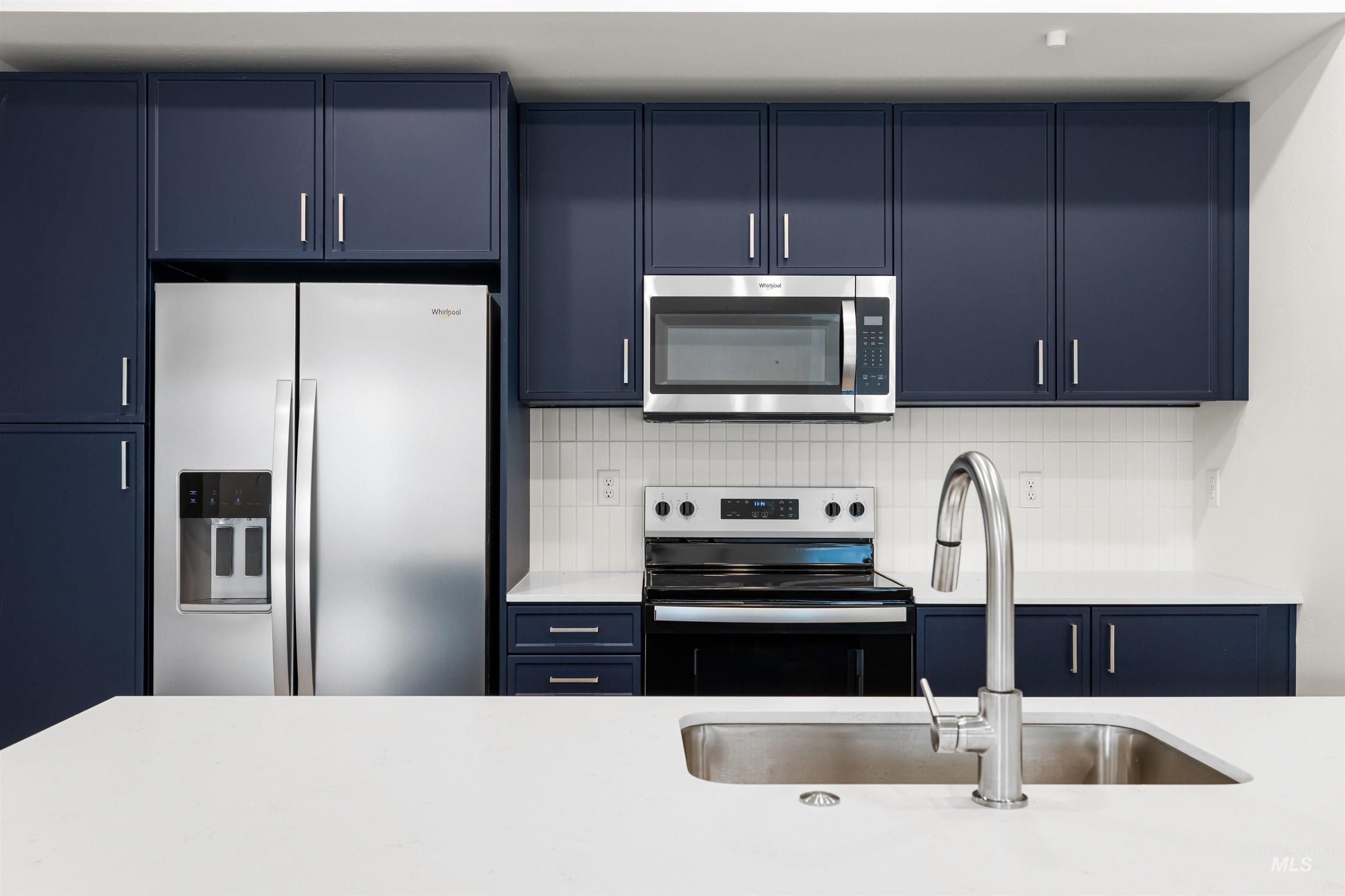 Kitchen with blue cabinets, stainless steel appliances, tasteful backsplash, and light stone countertops