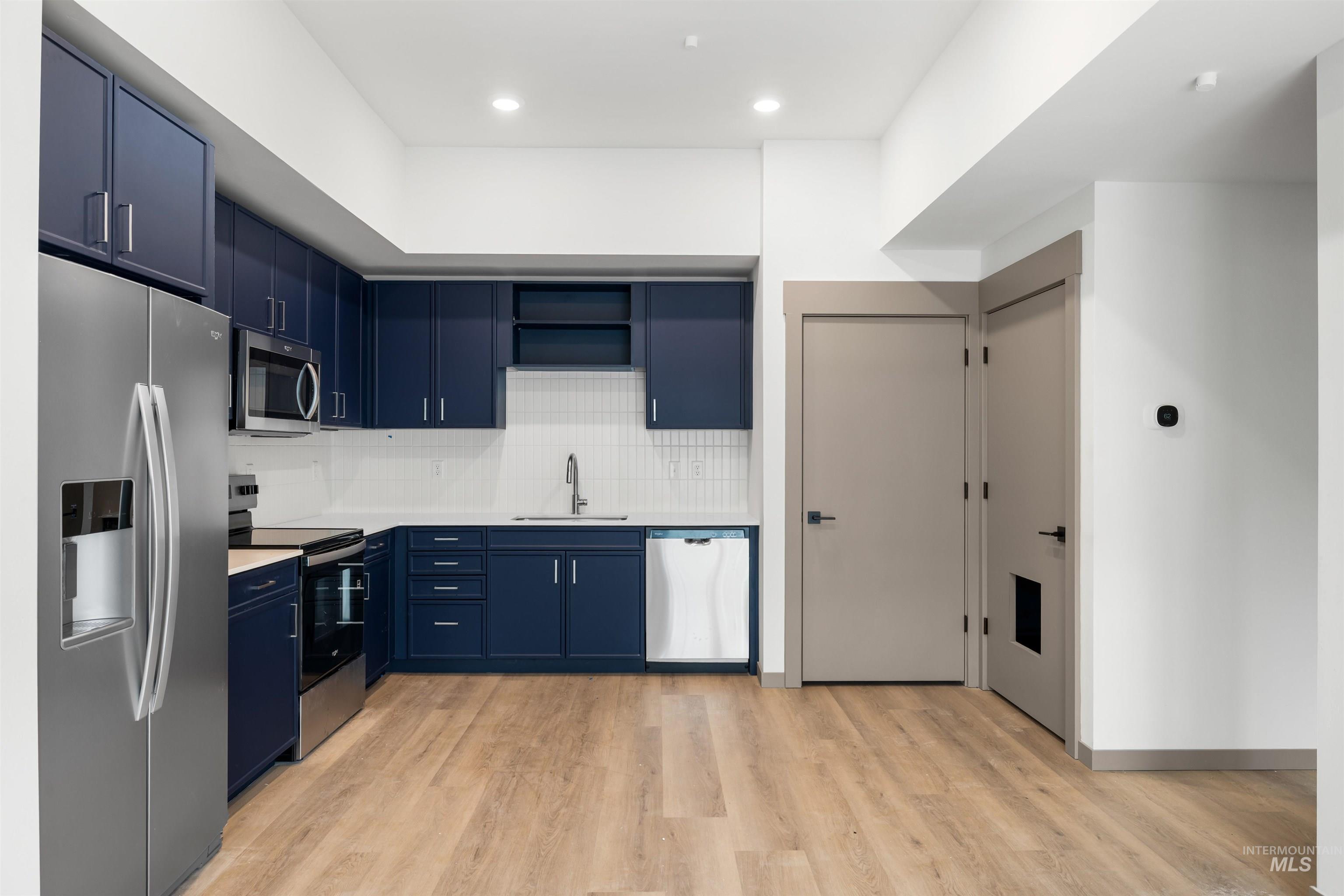 Kitchen featuring blue cabinets, stainless steel appliances, tasteful backsplash, light wood finished floors, and open shelves