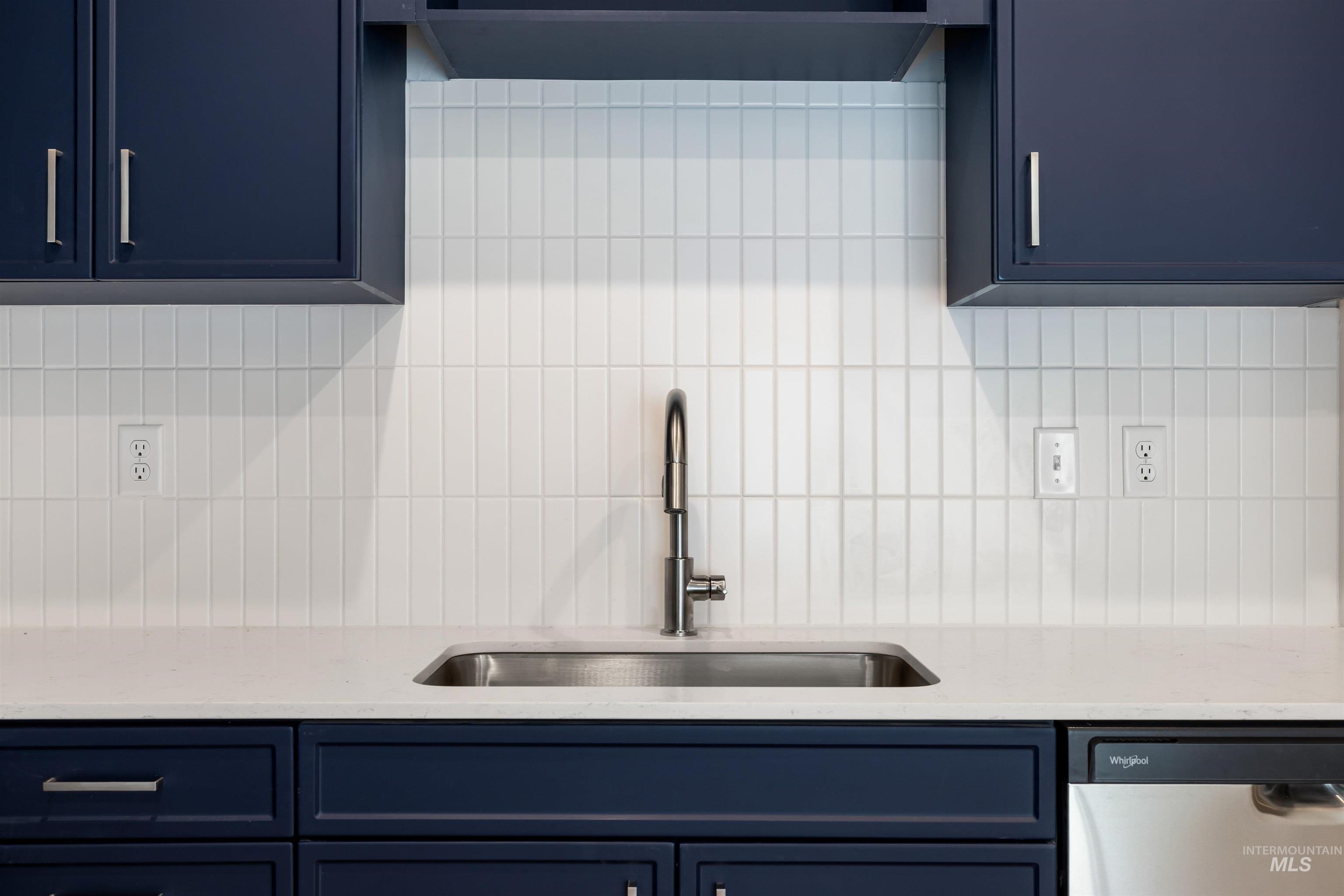 Kitchen with blue cabinets, decorative backsplash, dishwasher, and light stone counters