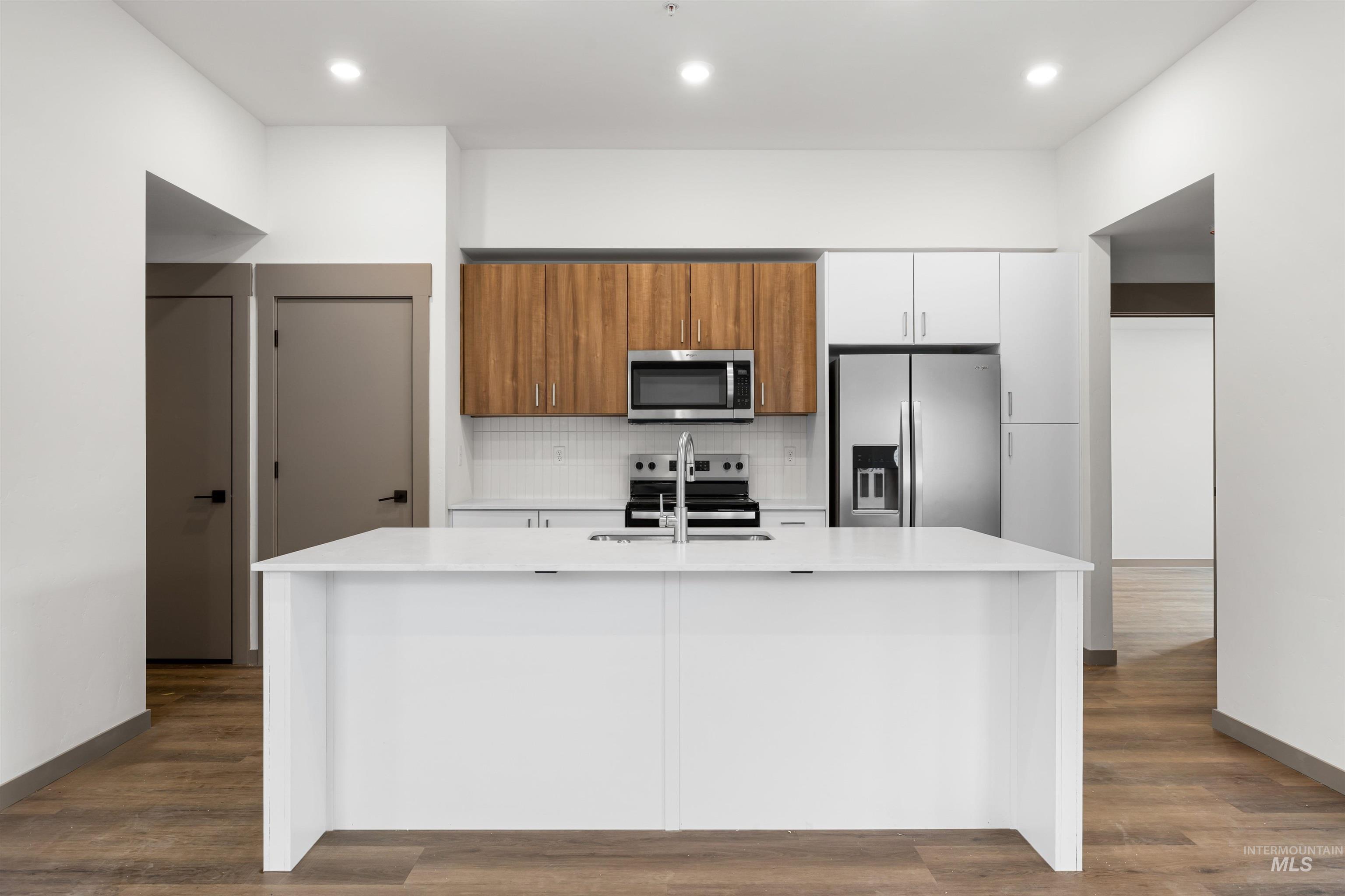 Kitchen featuring appliances with stainless steel finishes, backsplash, white cabinetry, brown cabinetry, and modern cabinets