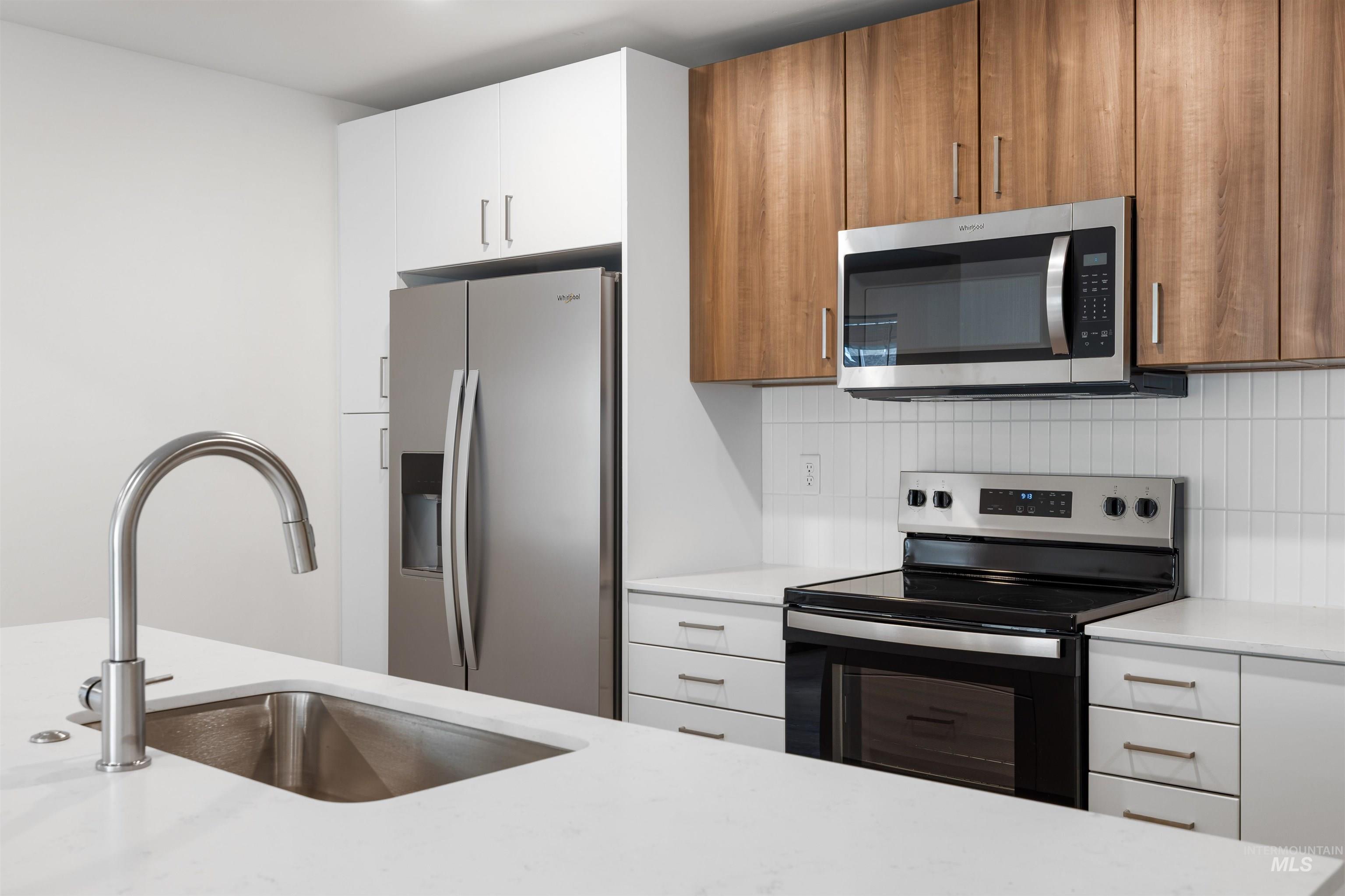 Kitchen with stainless steel appliances, backsplash, light stone counters, brown cabinetry, and modern cabinets