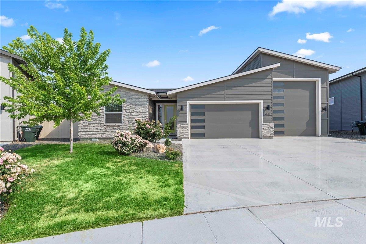 View of front of house featuring an attached garage, stone siding, a front yard, and driveway