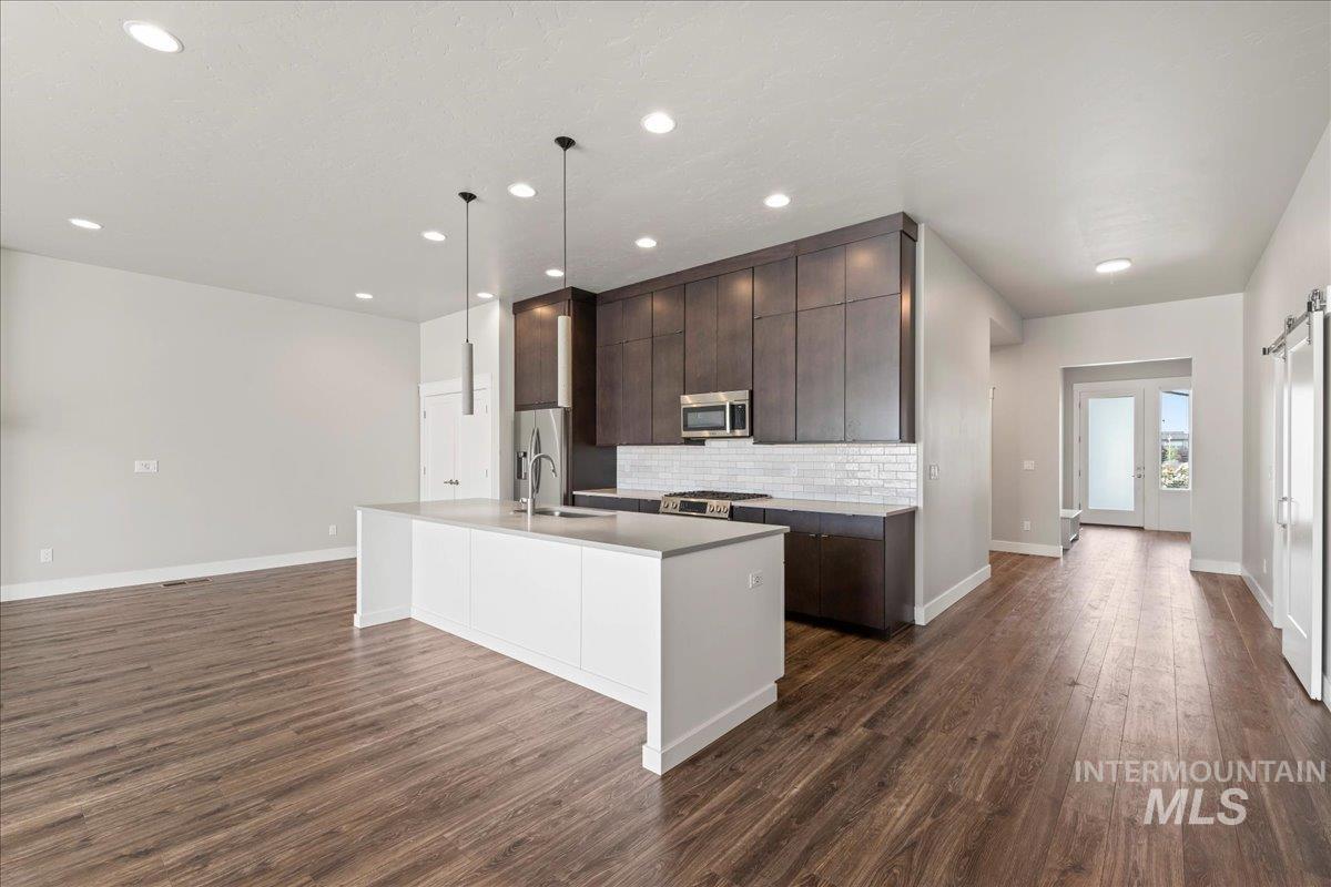 Kitchen with dark brown cabinets, tasteful backsplash, a kitchen island with sink, dark wood-type flooring, and appliances with stainless steel finishes