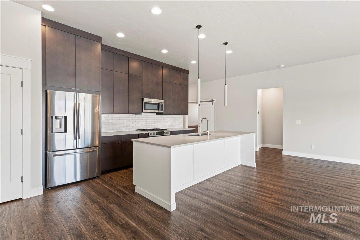 Kitchen featuring stainless steel appliances, dark brown cabinets, tasteful backsplash, dark wood-style floors, and modern cabinets