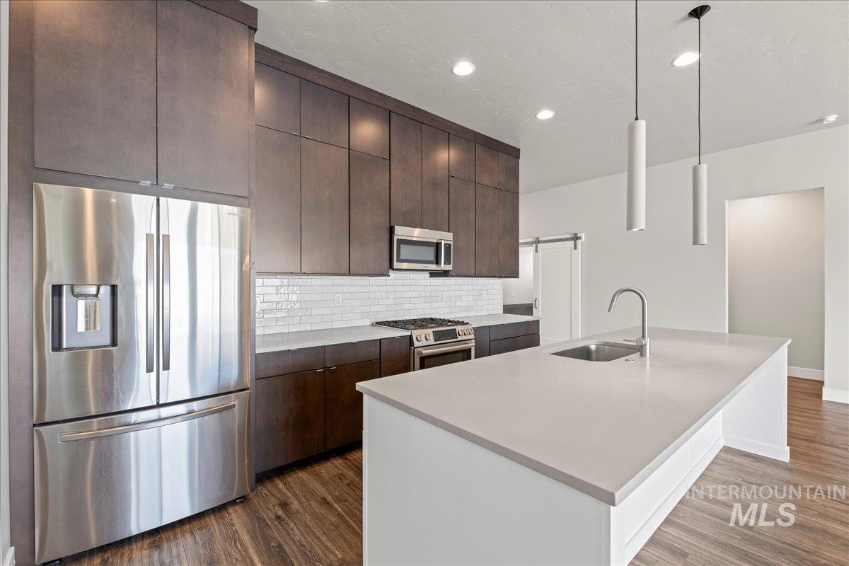 Kitchen featuring appliances with stainless steel finishes, dark wood-type flooring, dark brown cabinetry, decorative backsplash, and light countertops