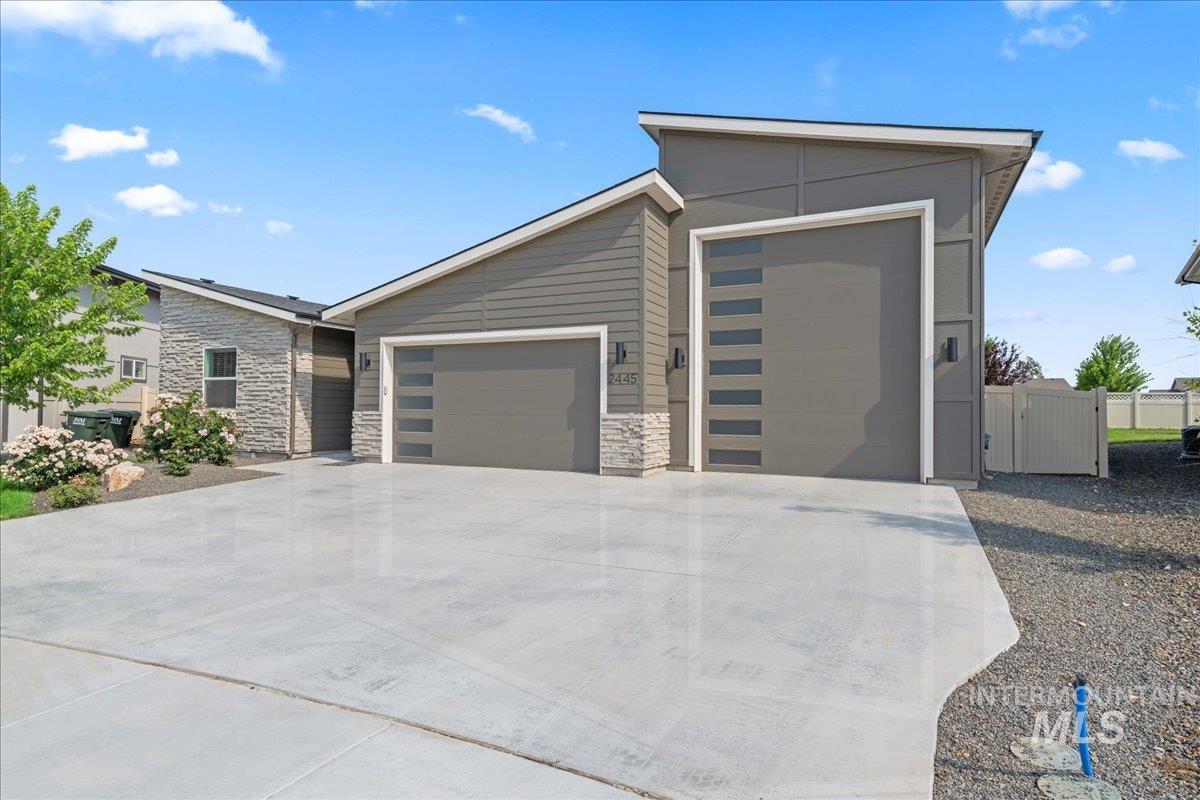 Contemporary home with a garage, stone siding, driveway, and a gate