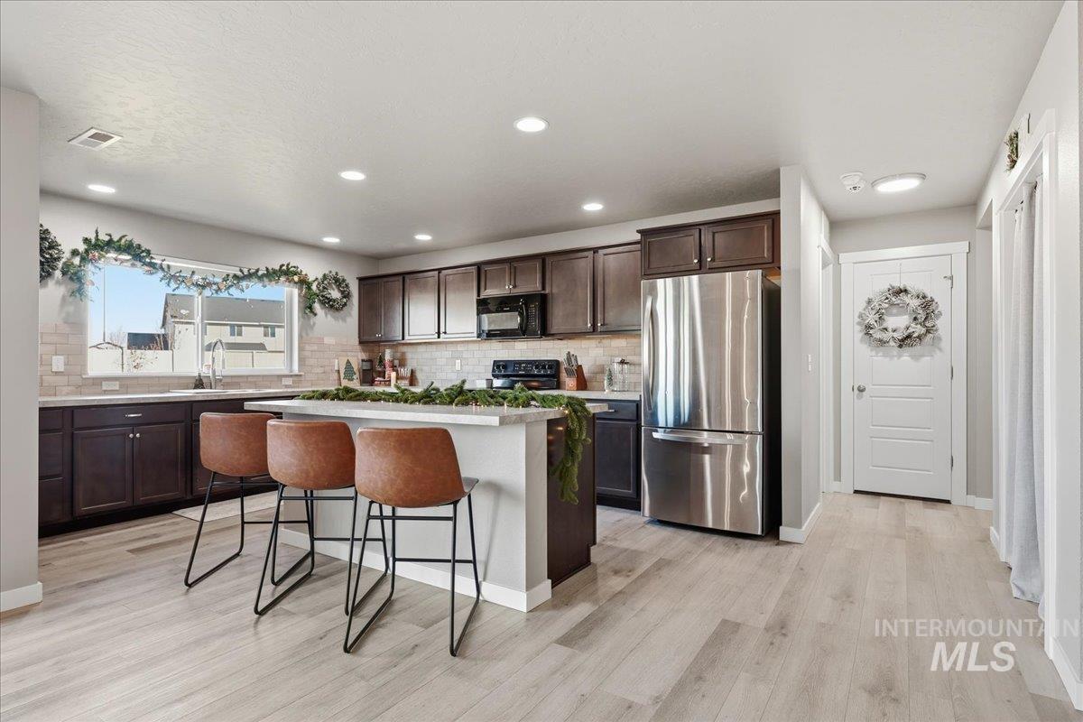 Kitchen featuring a kitchen breakfast bar, dark brown cabinetry, light countertops, black appliances, and a center island