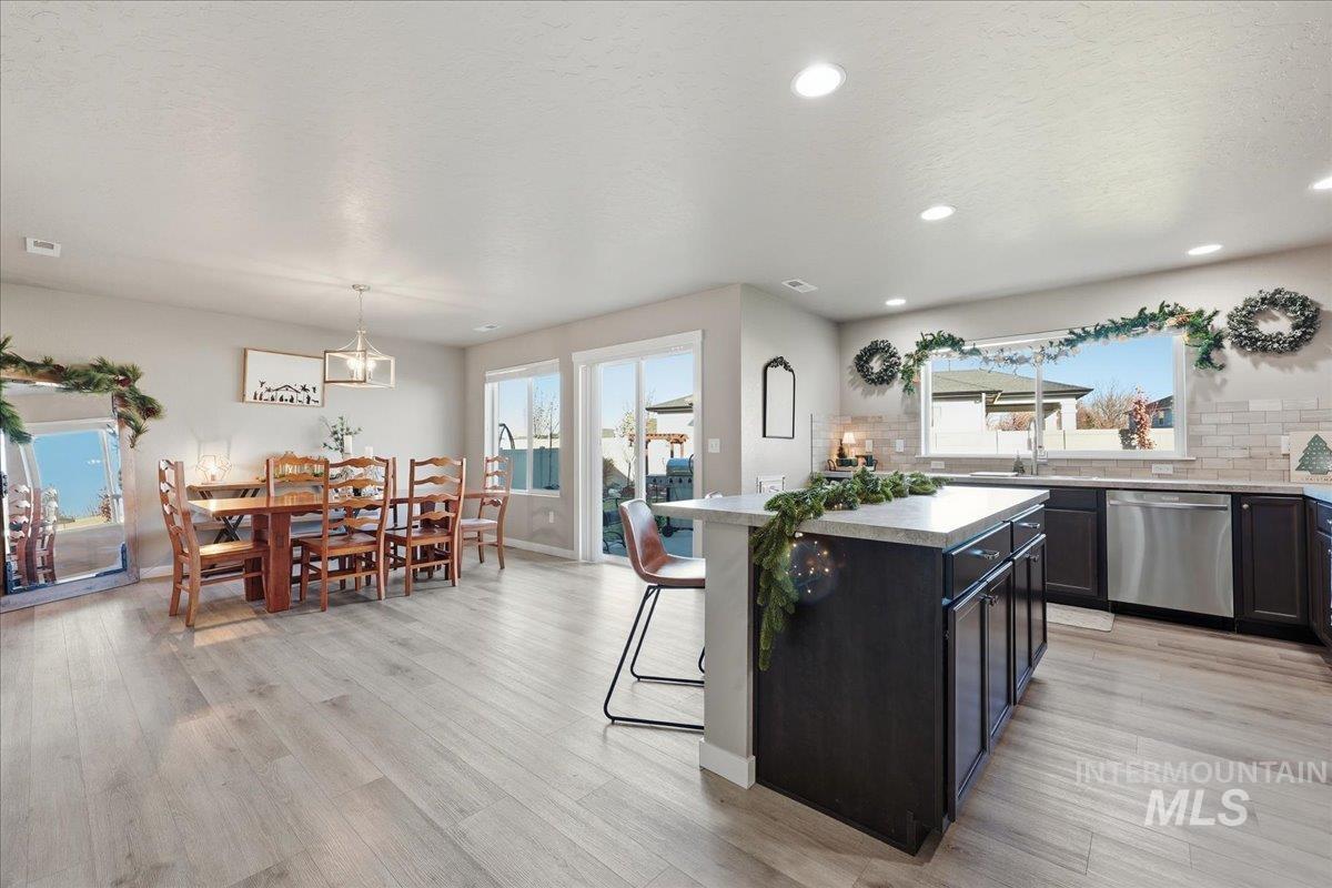 Kitchen with a center island, dishwasher, backsplash, light wood-type flooring, and a kitchen breakfast bar