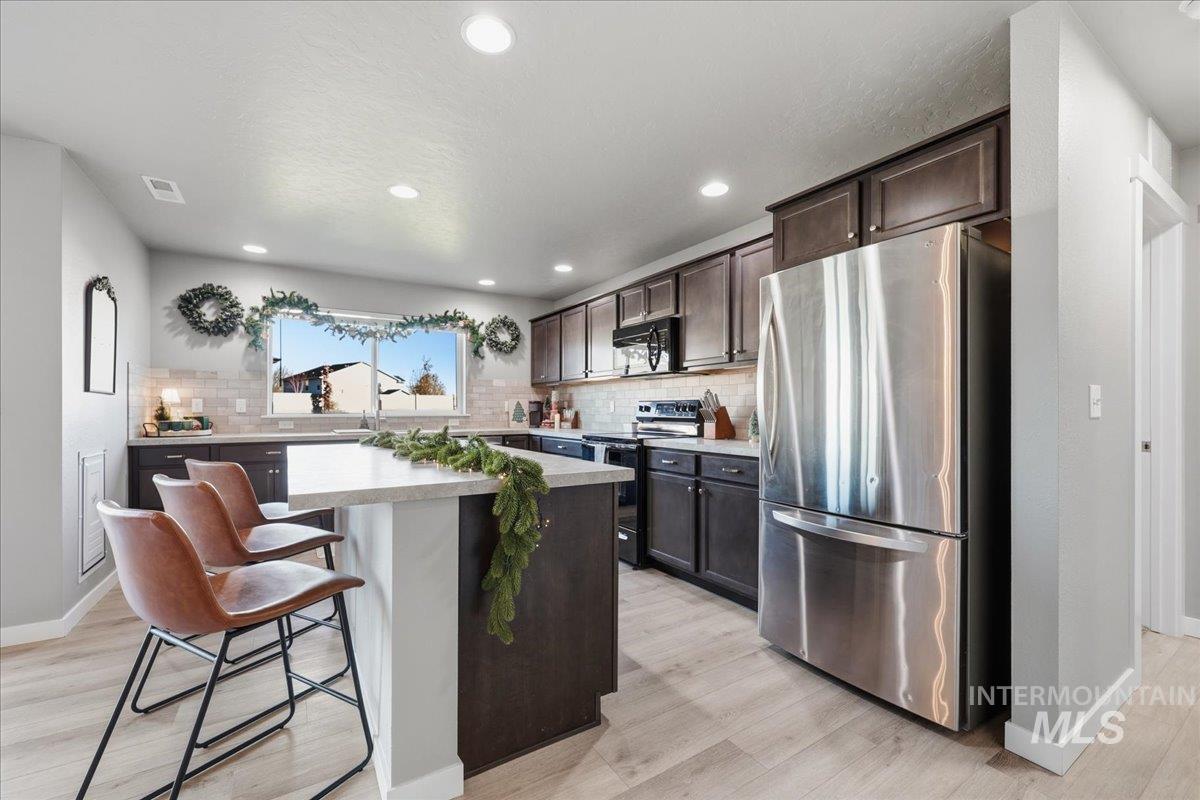 Kitchen featuring black appliances, a kitchen breakfast bar, dark brown cabinets, a kitchen island, and light wood finished floors