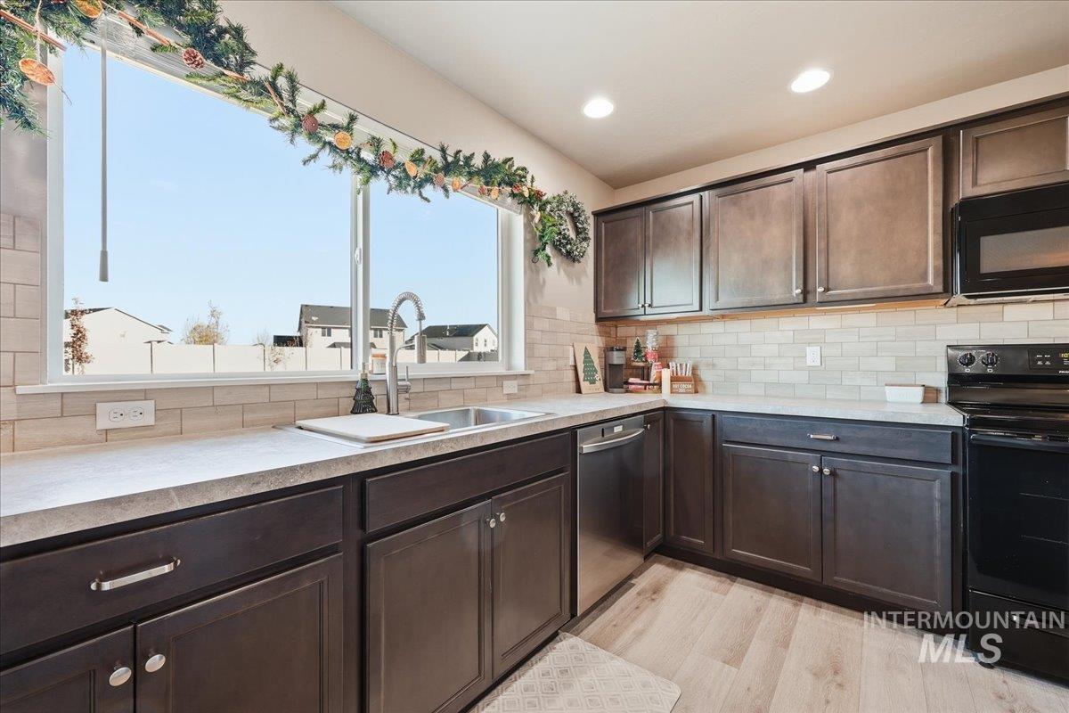 Kitchen featuring dark brown cabinetry, black appliances, light wood finished floors, decorative backsplash, and light stone counters