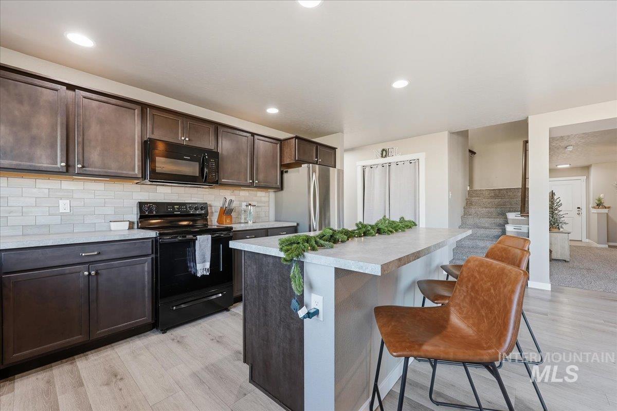 Kitchen with dark brown cabinets, light countertops, black appliances, a kitchen breakfast bar, and a center island
